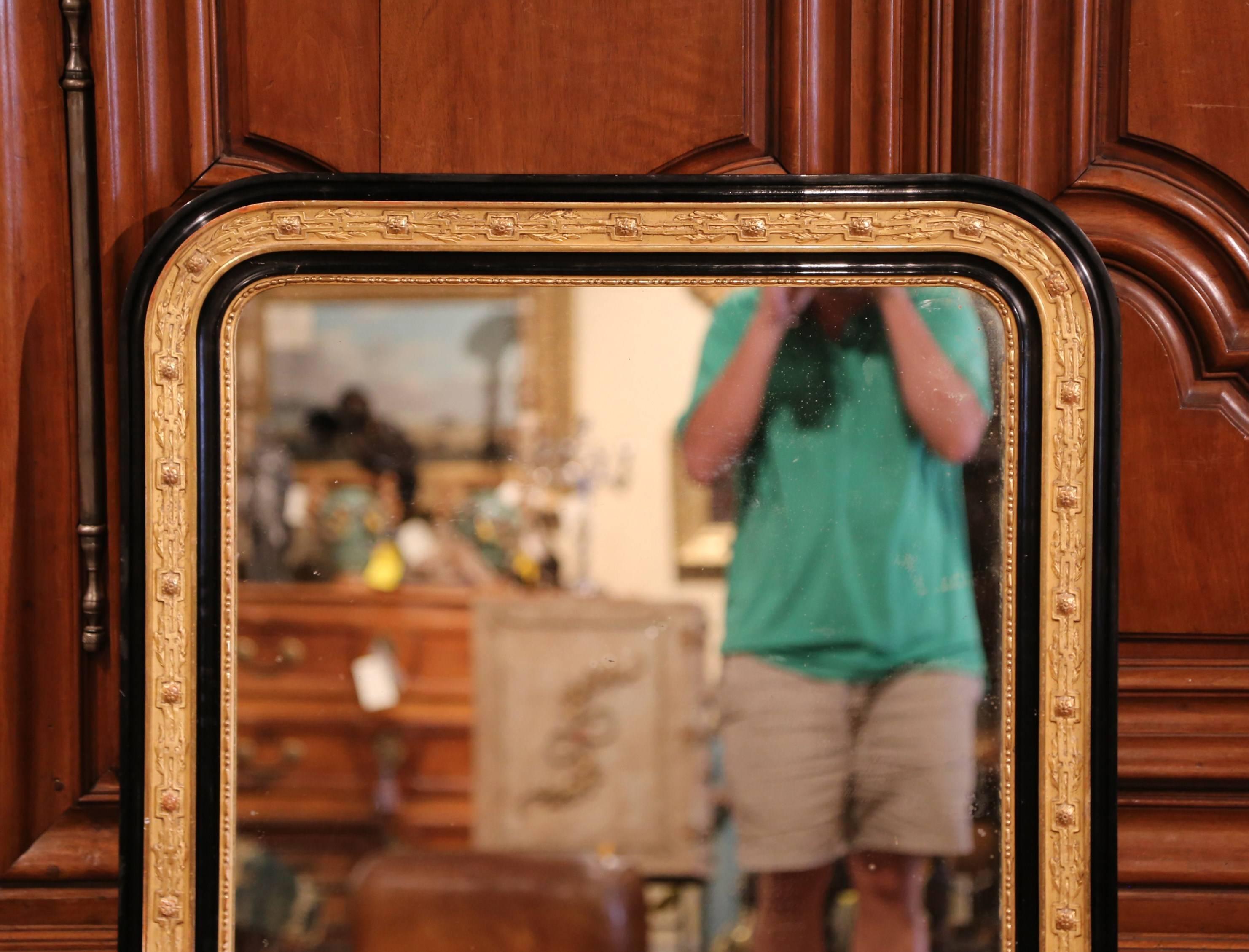 This elegant antique two-tone gold leaf and black lacquered mirror was crafted in France, circa 1870. The large frame is embellished with hand carved and raised leaf and floral decor all around. The French wall hanging piece is in excellent