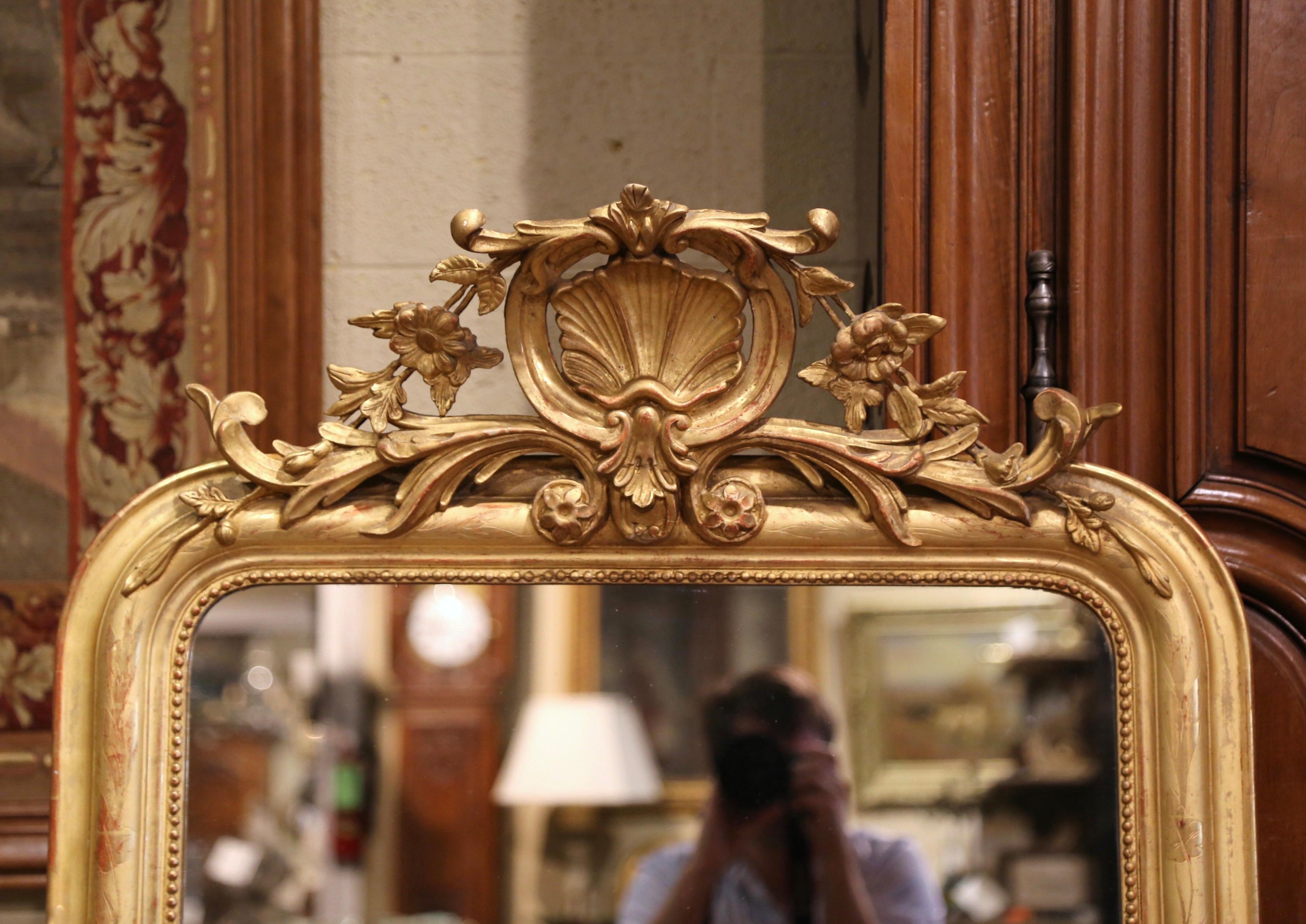 This elegant, antique wall mirror was crafted in France, circa 1870. Rectangular in shape and over five feet tall, the large mirror is decorated at the pediment with a large cartouche shell in the center flanked with carved floral and leaf motifs on