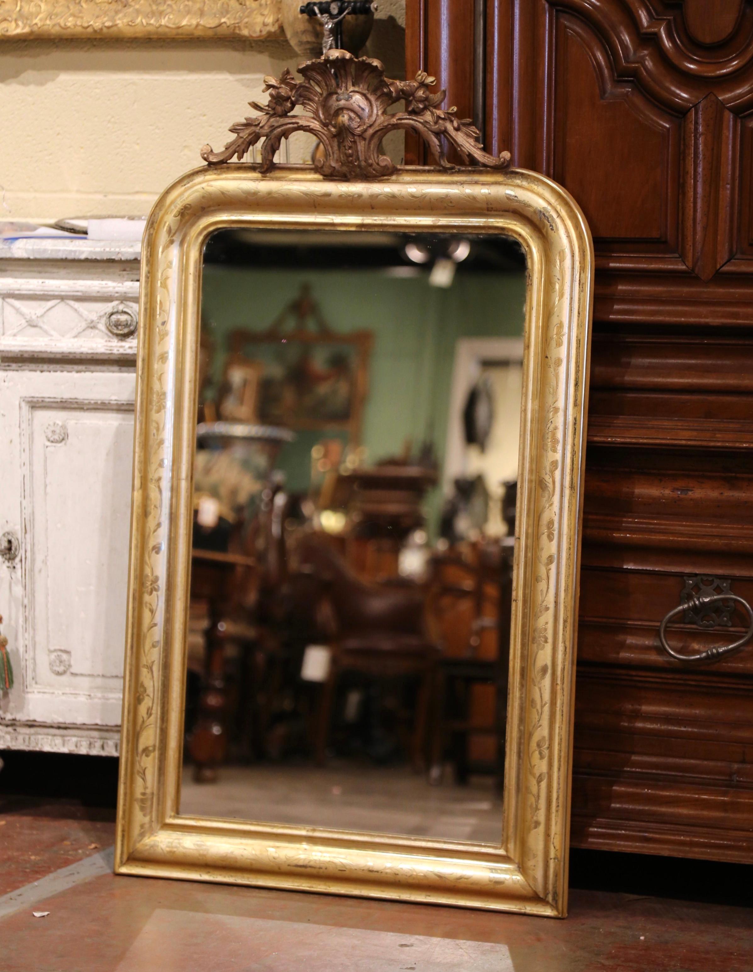 This elegant, antique wall mirror was crafted in France, circa 1870. The wall decor features a large shell cartouche at the pediment flanked with carved foliate motifs on the sides. The gilt frame, dressed with the original inside mercury glass, is
