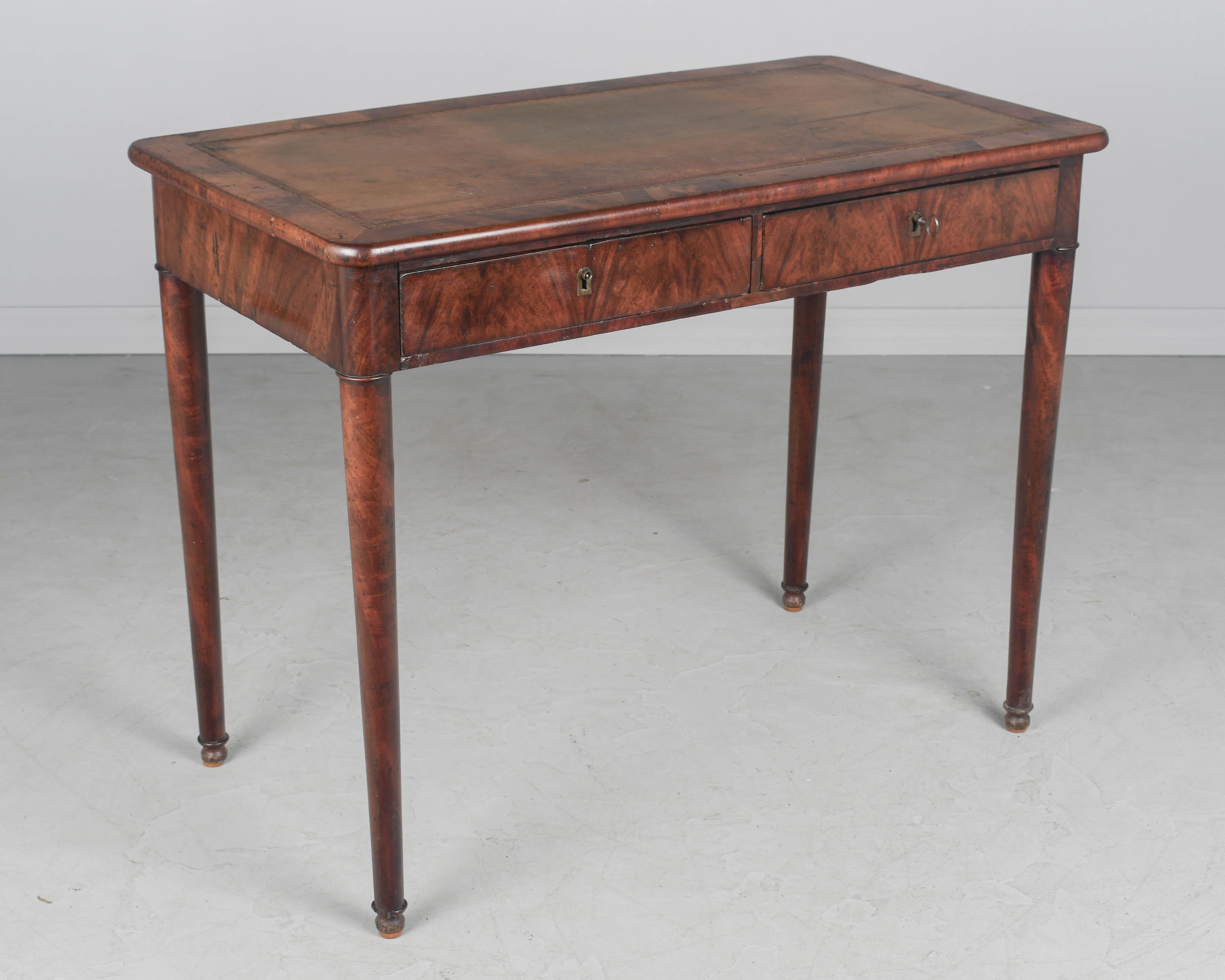 A 19th century French Louis Philippe style bureau plat, or desk, made of solid and veneer of mahogany. Two dovetailed drawers with working locks and one key. Leather top with gold embossed trim. Turned tapered legs with ball feet. Sturdy and