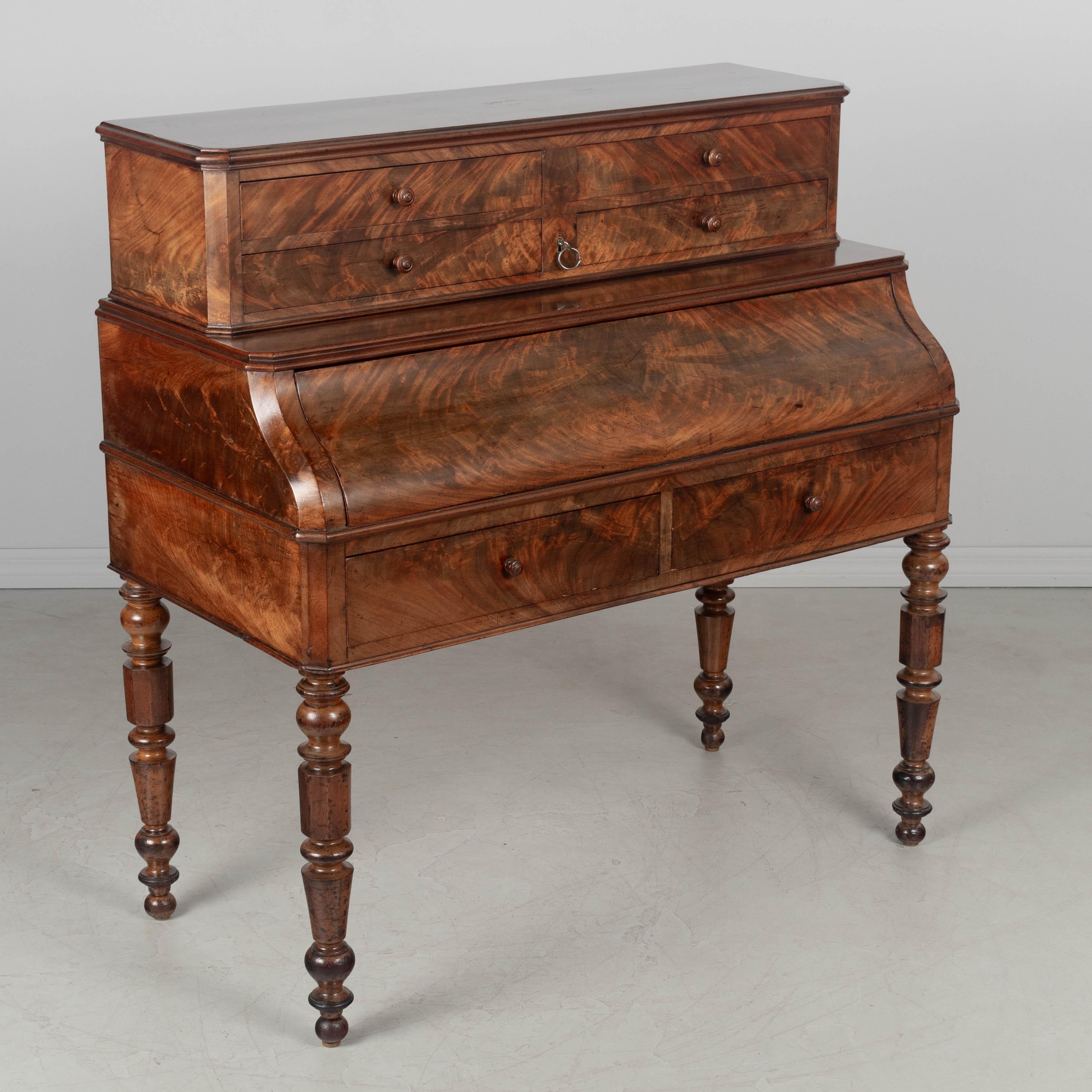 Escritorio francés de caoba Louis Philippe de principios del siglo XIX con chapado de caoba flameada a juego y patas torneadas de caoba maciza. Este escritorio tiene un mecanismo de cierre en condiciones de funcionar con una llave. El frontal
