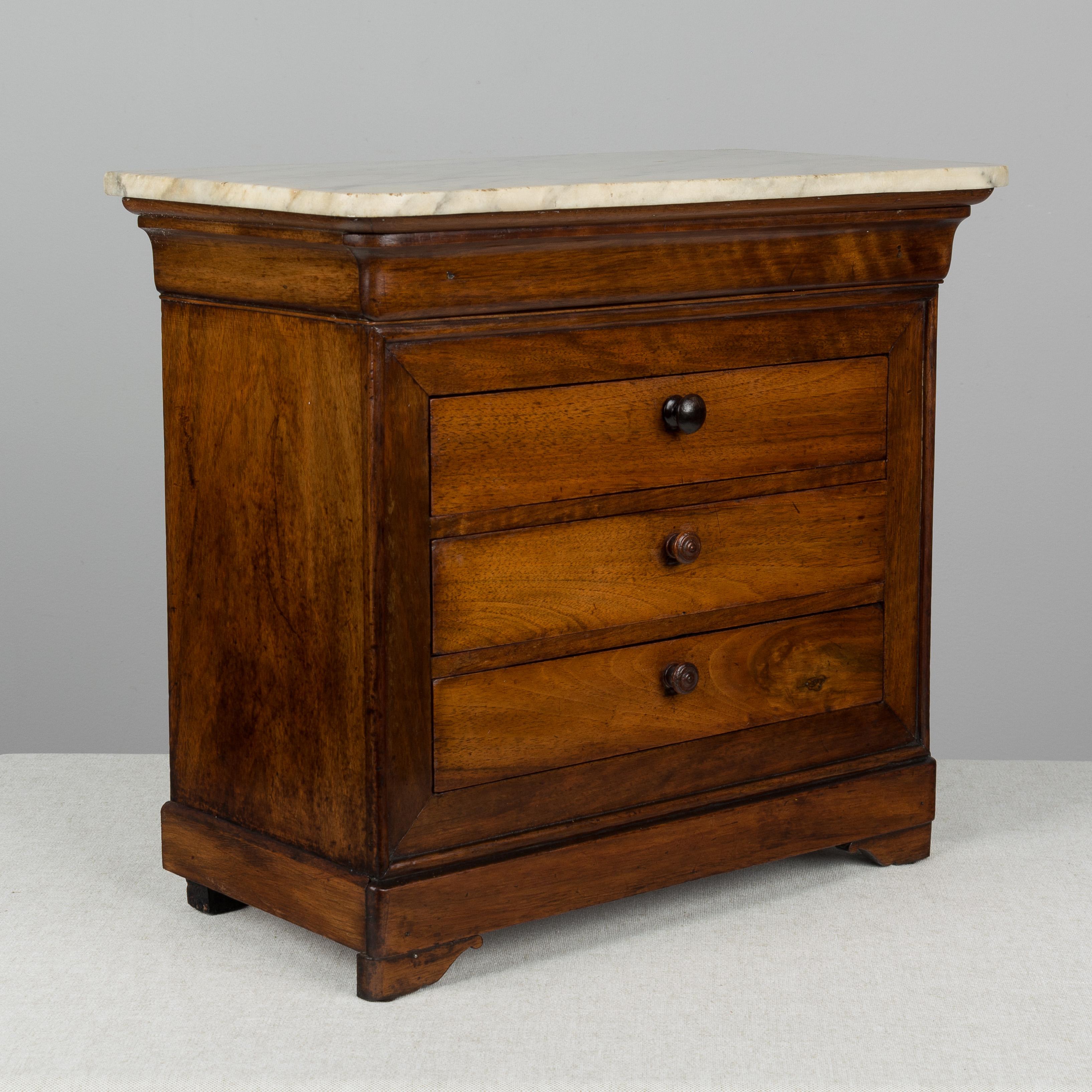 A 19th century Louis Philippe miniature sample commode made of solid walnut with French polish finish. Three dovetailed drawers with turned knobs and one hidden top drawer. The top knob is different than the others. Original marble top. Pine as a