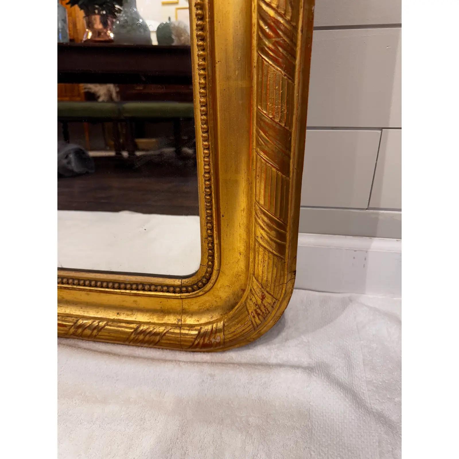 A large and striking example of a timeless classic, this French Louis Philippe mirror is embellished with a large floral and foliate crest. This mirror is adorned with a repeating gilt wood border, pairing well with the massive crest. It has a rich