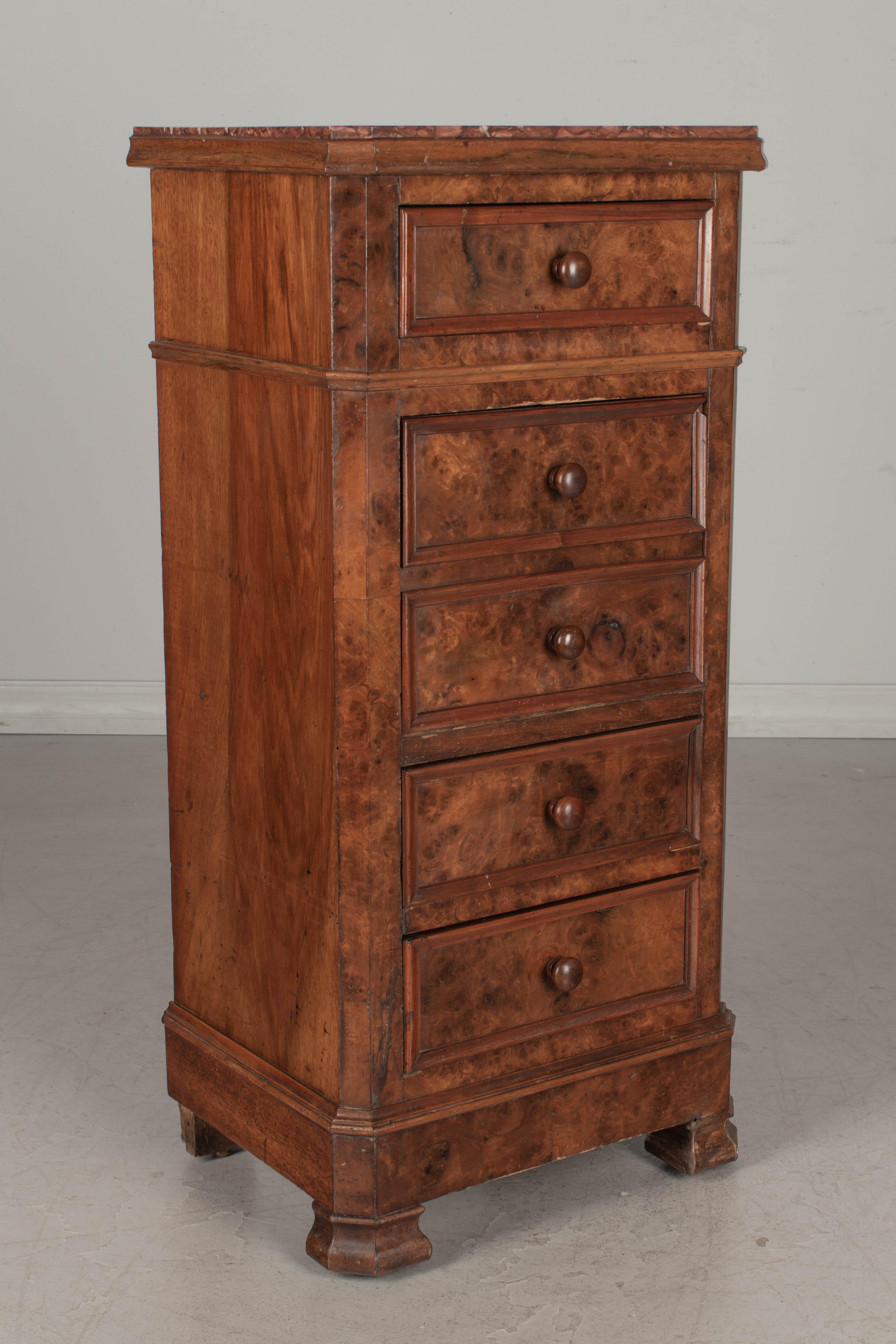 A 19th century French bedside table, or nightstand, made of walnut with veneer of burled walnut front. Three dovetailed drawers and a door that hinges open to reveal an interior compartment, once used to store a chamber pot. Original red veined