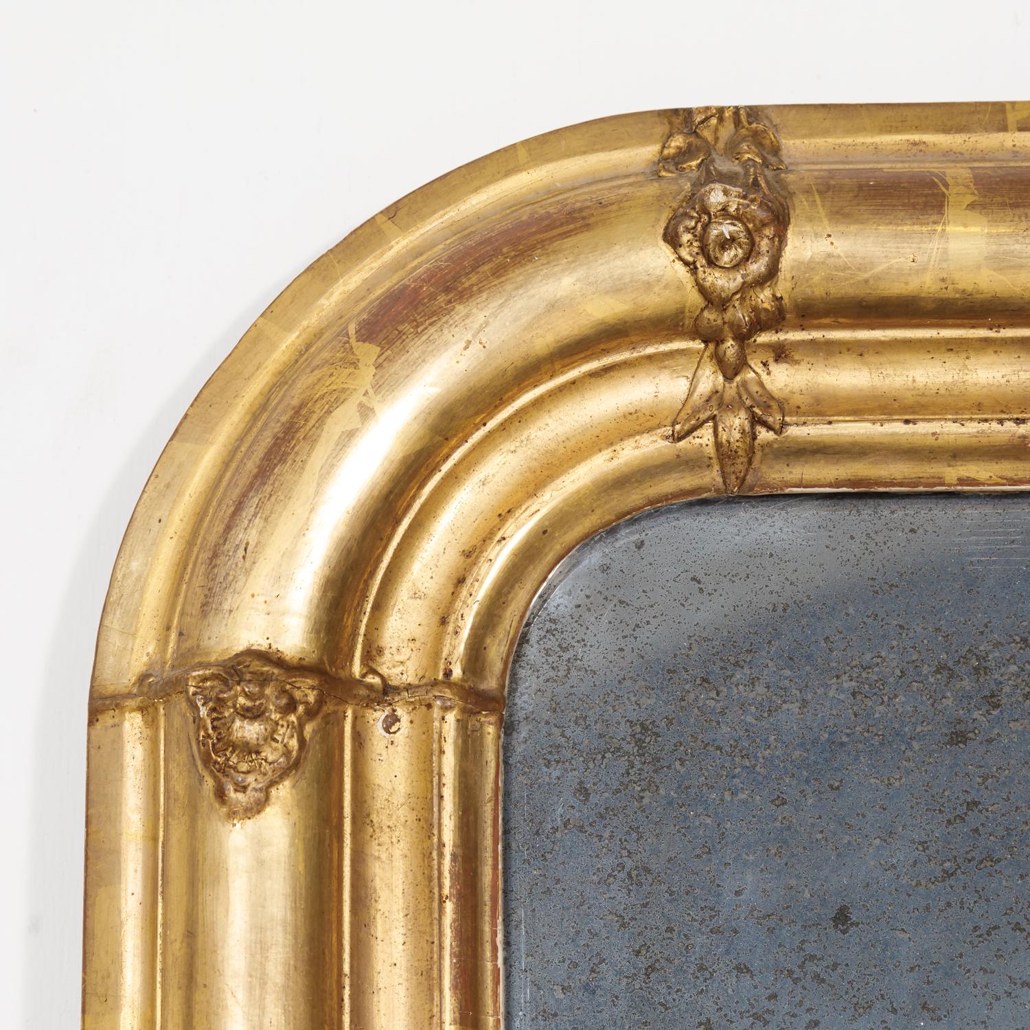 19th century French period Louis Philippe giltwood mirror adorned with floral and foliate carvings, having its original mercury glass, circa 1830s.The rectangular shape of the frame has straight corners at the base, while the upper shoulders have