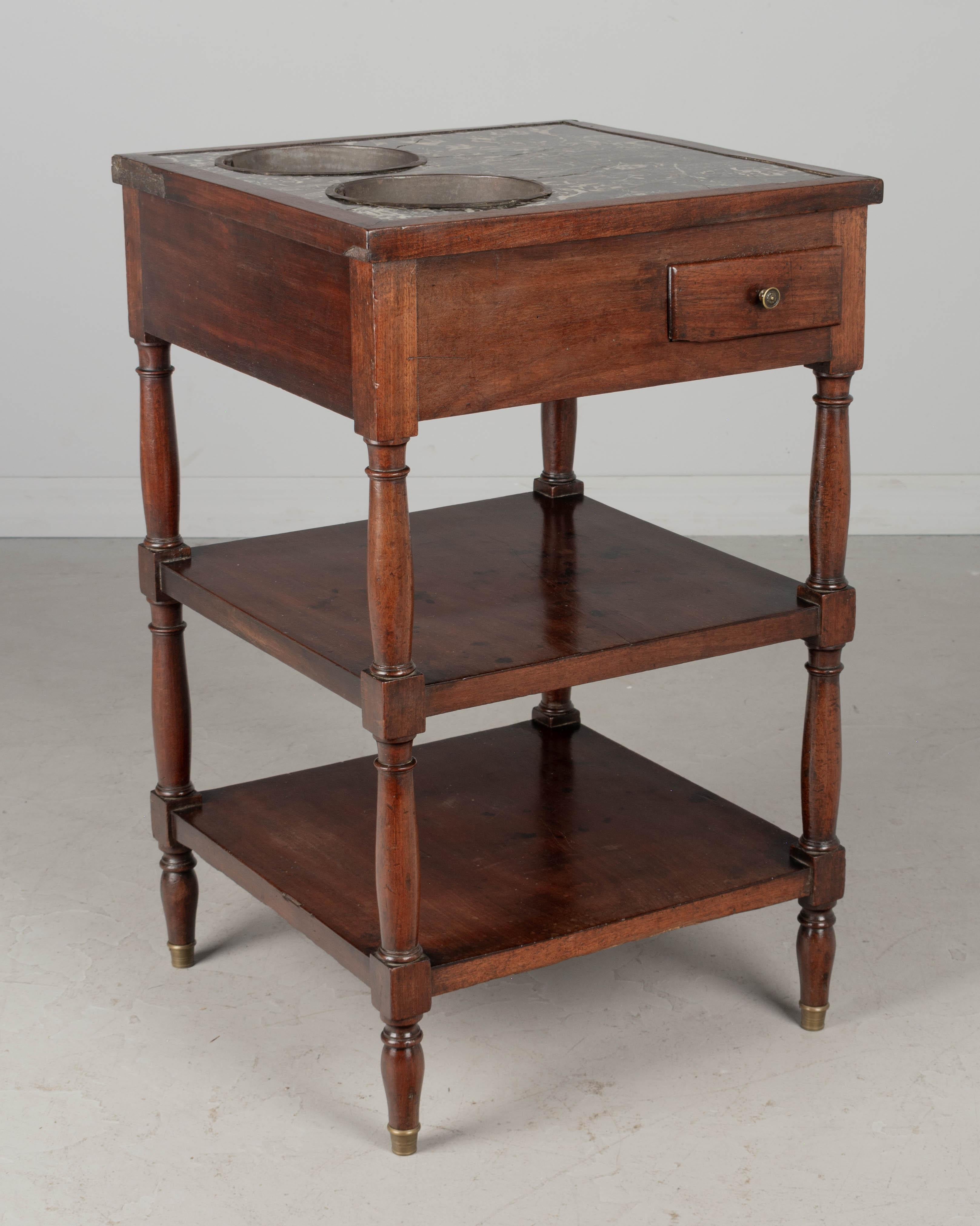 A 19th century Louis Philippe French rafraîchissoir, or side table with wine coolers, made of solid and veneer of walnut with turned legs, two shelves and a small dovetailed drawer. Original gray St. Anne marble top with two inset zinc wine buckets.