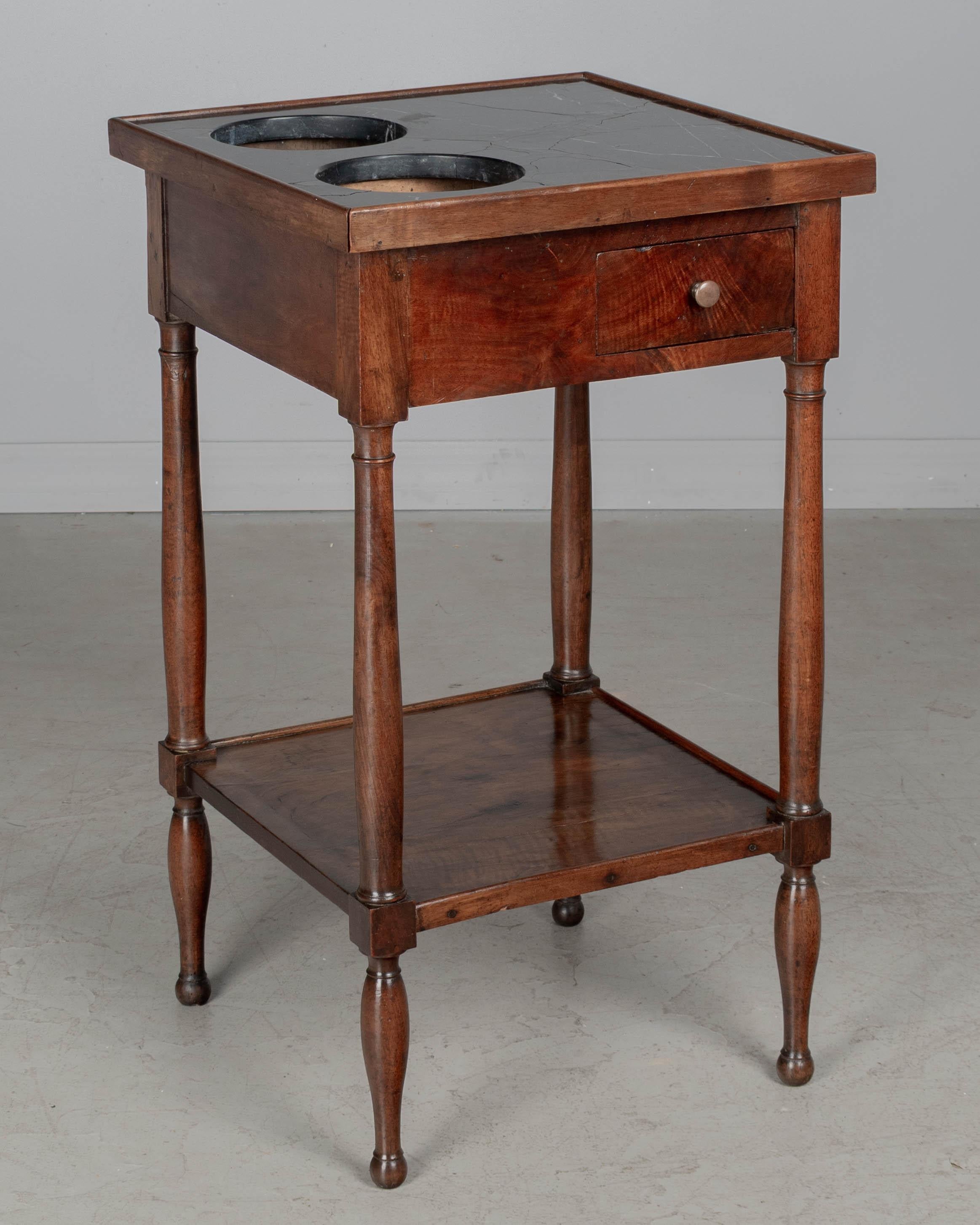 A 19th century French Louis Philippe rafraîchissoir, or wine cooler, made of walnut with turned legs, lower shelf and a small dovetailed drawer with brass knob. Black marble top with two cut-outs to hold wine buckets (missing). Marble is cracked but