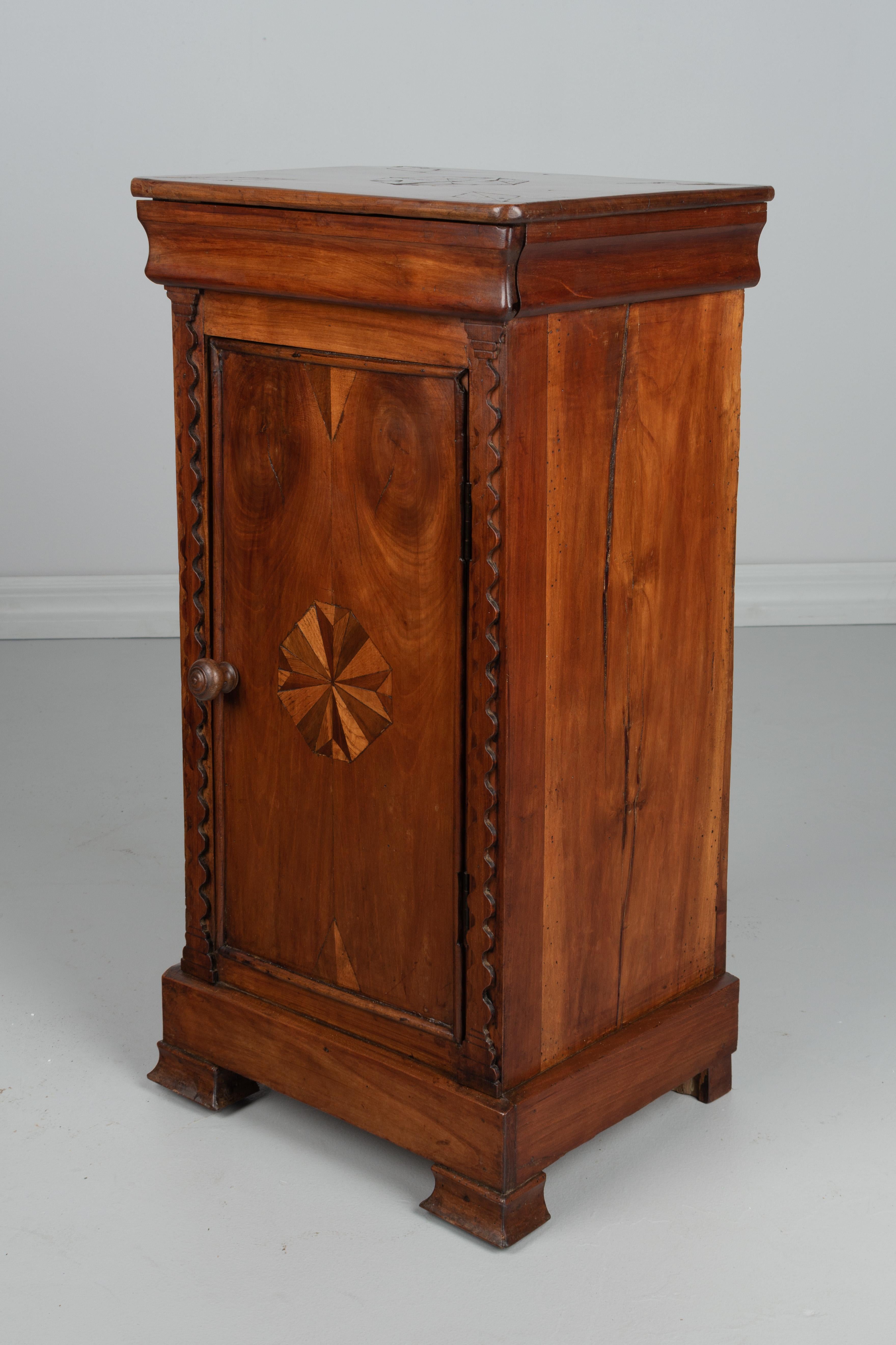 An early 19th century French Louis Philippe nightstand or side table made of solid cherry with simple marquetry inlaid decoration. Hidden drawer above a cabinet door. One interior shelf. Finely crafted for a country table. Waxed finish. Minor