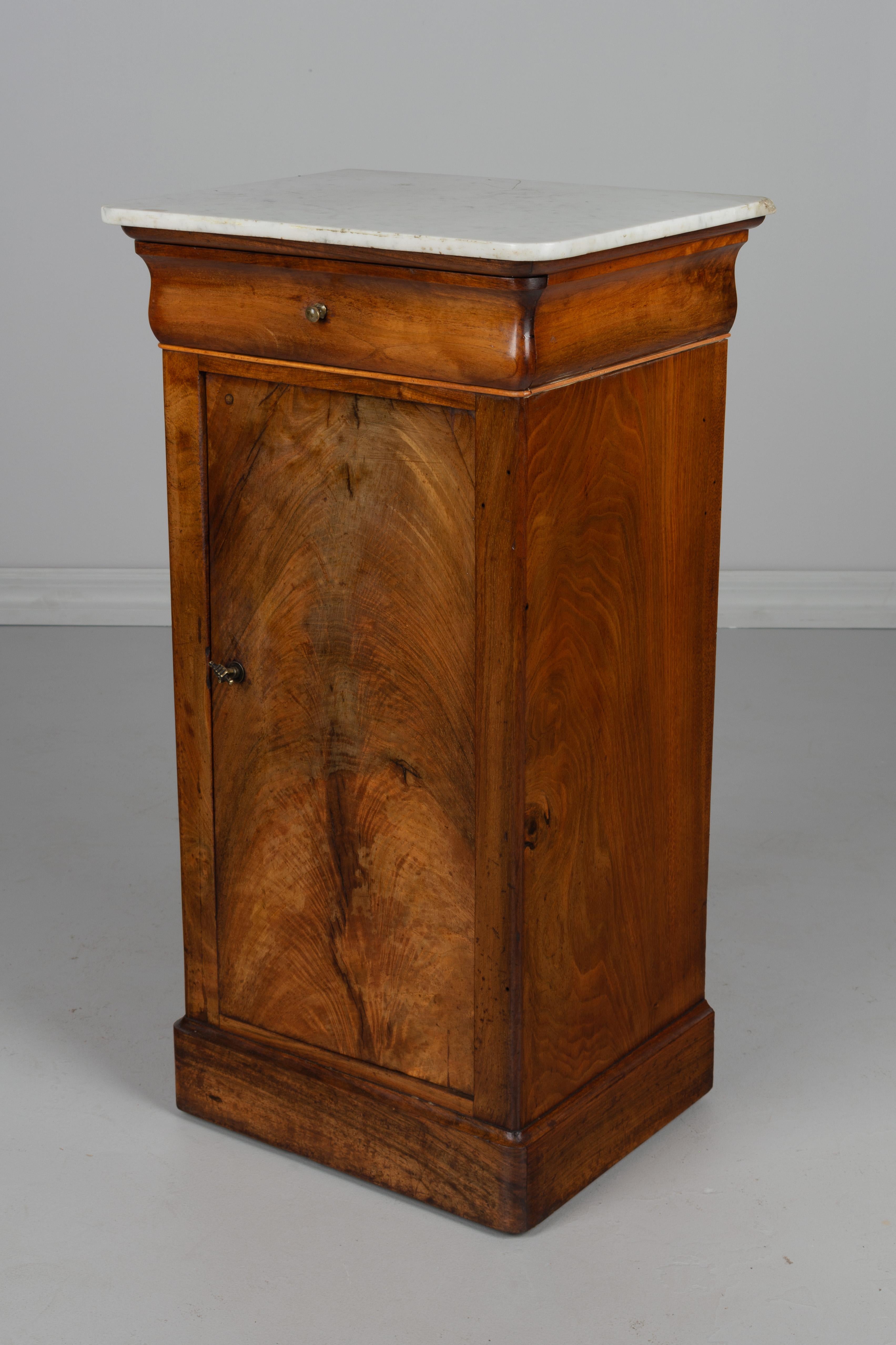 A 19th century Louis Philippe side table made of veneer of walnut with French polish finish. Door with cast hand knob opens to a single shelf. Drawer with small brass knob. White marble a fixed to the top. In good original condition with a small