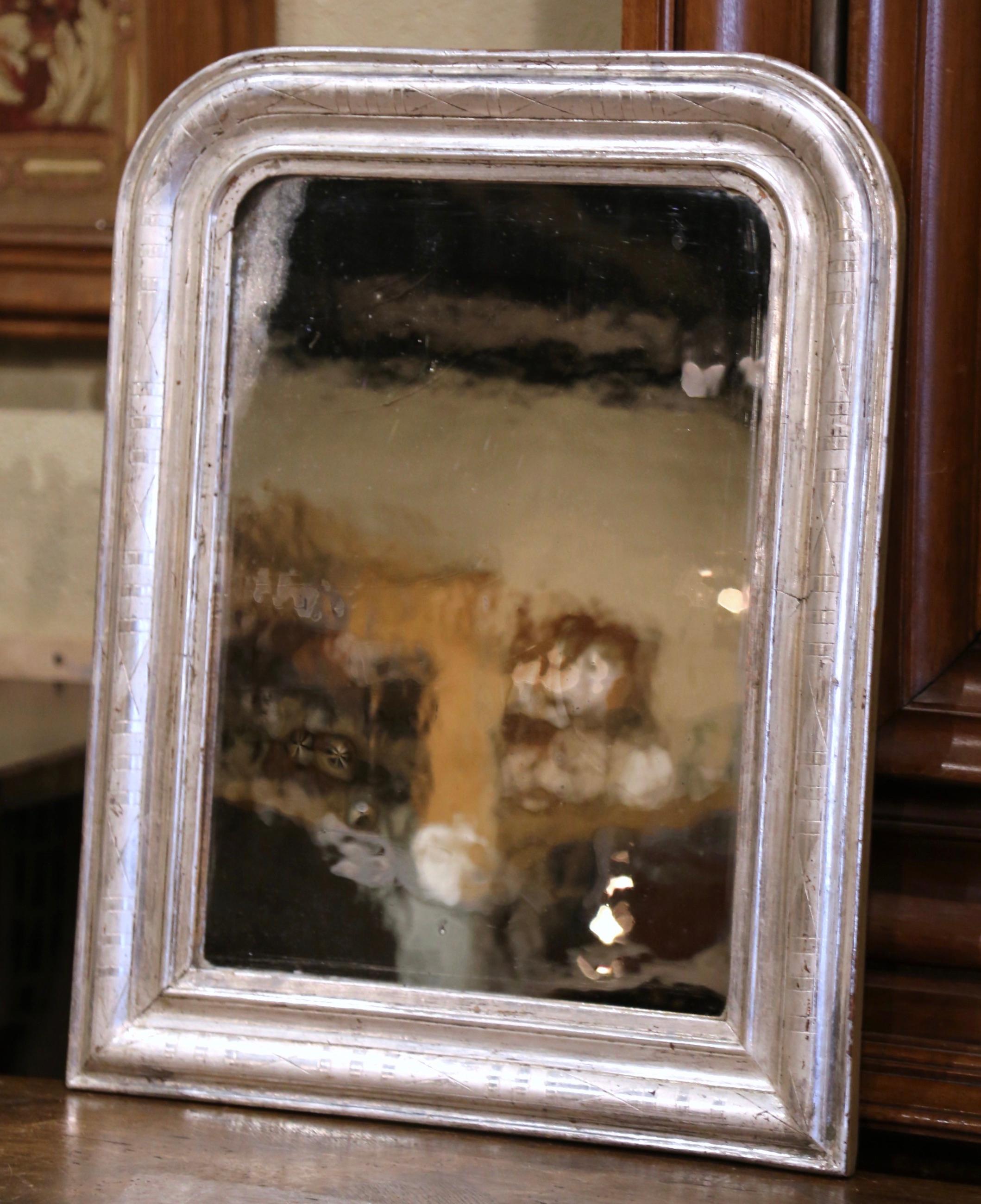 Crafted in the Burgundy region of France, circa 1870, the small antique mirror has traditional, timeless lines with rounded corners. The elegant frame is decorated with a luxurious silver leaf finish, further embellished with an engraved two-tone