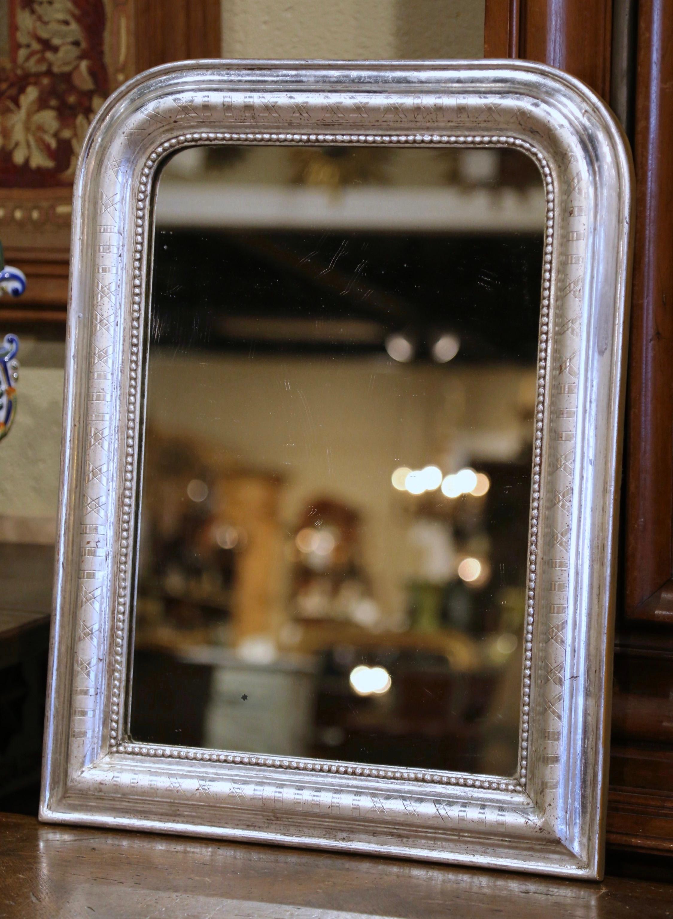 Crafted in the Burgundy region of France, circa 1870, the petite antique mirror has traditional, timeless lines with rounded corners. The elegant frame is decorated with a luxurious silver leaf finish, further embellished with an engraved two-tone