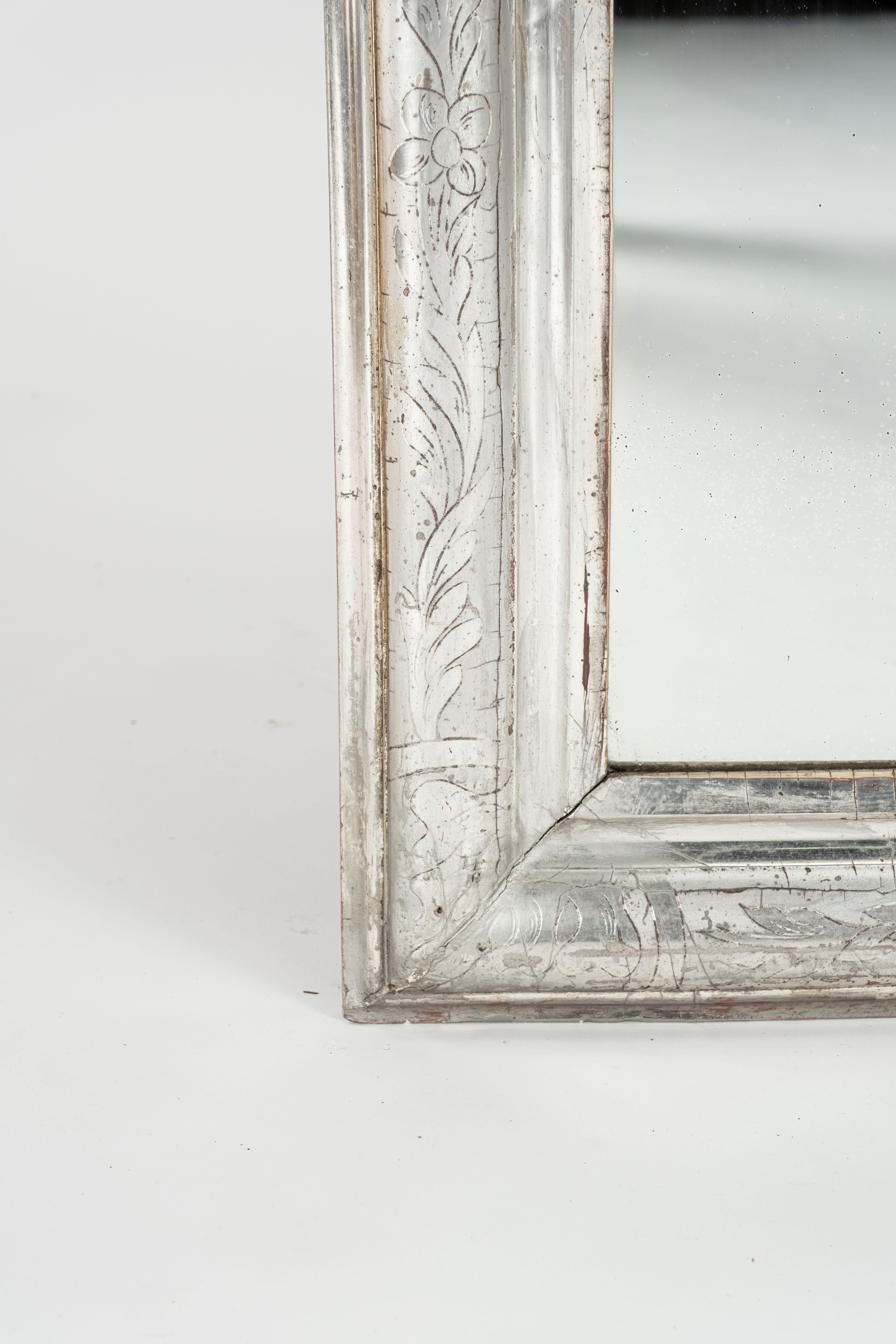 :A 19th century French silver leaf wall mirror. The frame to this pretty mirror has a decorative  design of entwining flowers and leaves etched into the surface, there are some rub marks and general historical wear as one would expect for the
