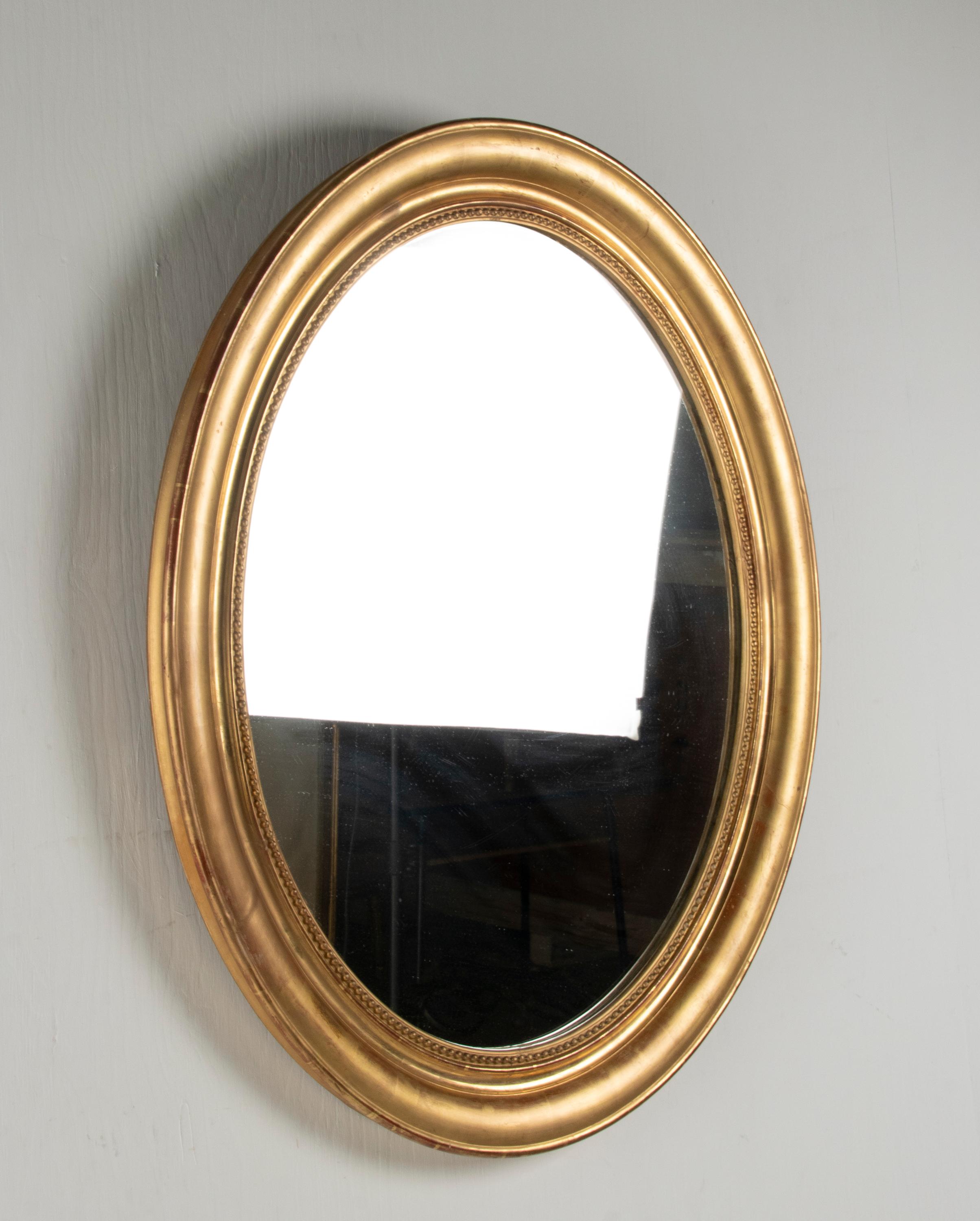 An antique French oval wall mirror, in beaded gilded frame. in Louis Philippe style, made in 1870-1880. The mirror is entirely gilded with gold leaf. The gold leaf has some wear, the underneath red bole gives a nice warm and antique patina. The