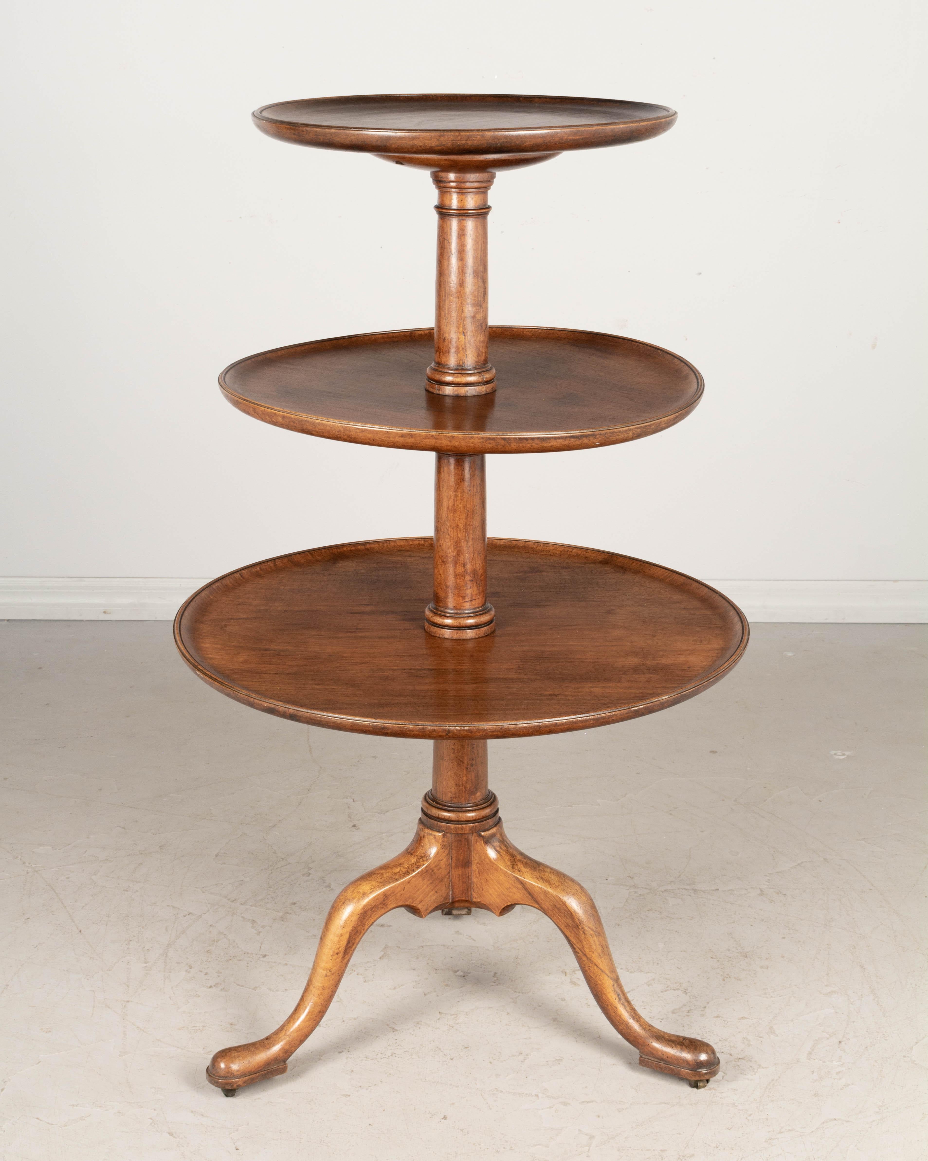 A 19th century French Louis Philippe style three-tier circular stand with turned center pole and tripod base with brass castors. Each shelf, or tray, is made from a single plank of walnut and will be dismantled for shipping. Middle tray is slightly