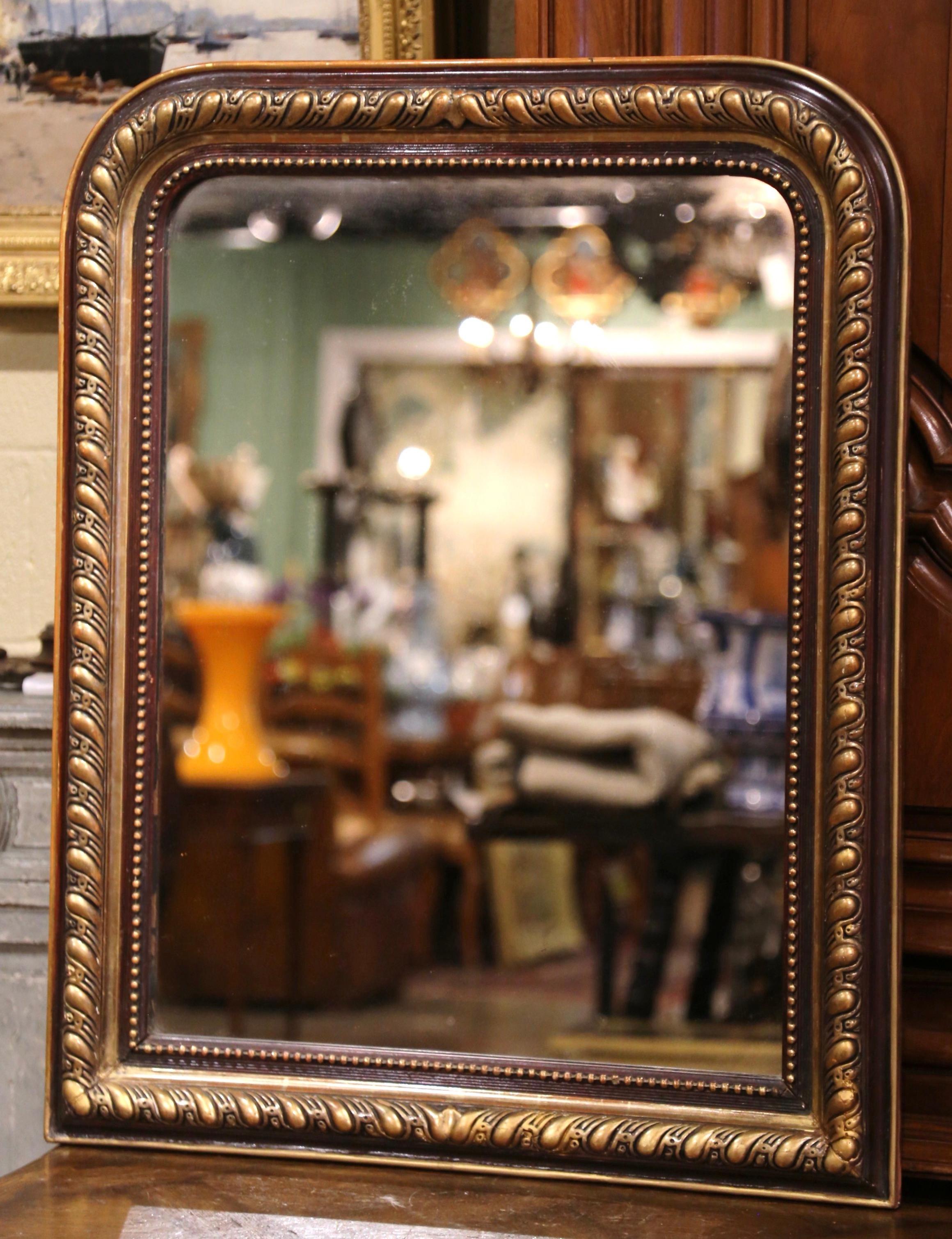 This elegant antique wall mirror was crafted in France, circa 1870. The two-tone frame is decorated with carved scroll motifs in high relief between patinated brown paint finish; the frame is further embellished with bead decor around the perimeter.