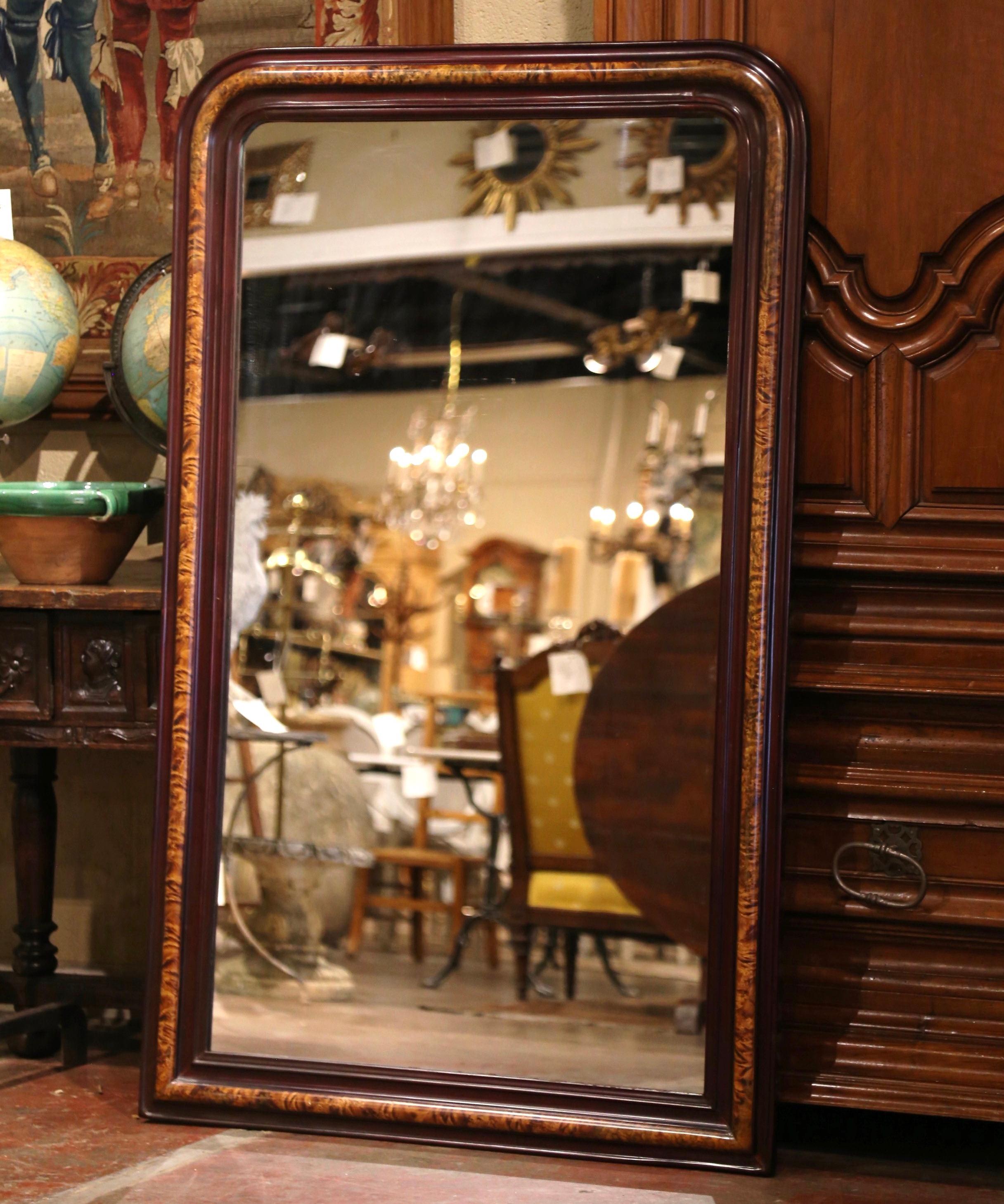 This elegant antique wall mirror was crafted in France, circa 1870. The tall frame is decorated with faux burl wood motifs in between patinated red paint finish. The large Louis Philippe two-tone mirror is in excellent condition with its mirrored