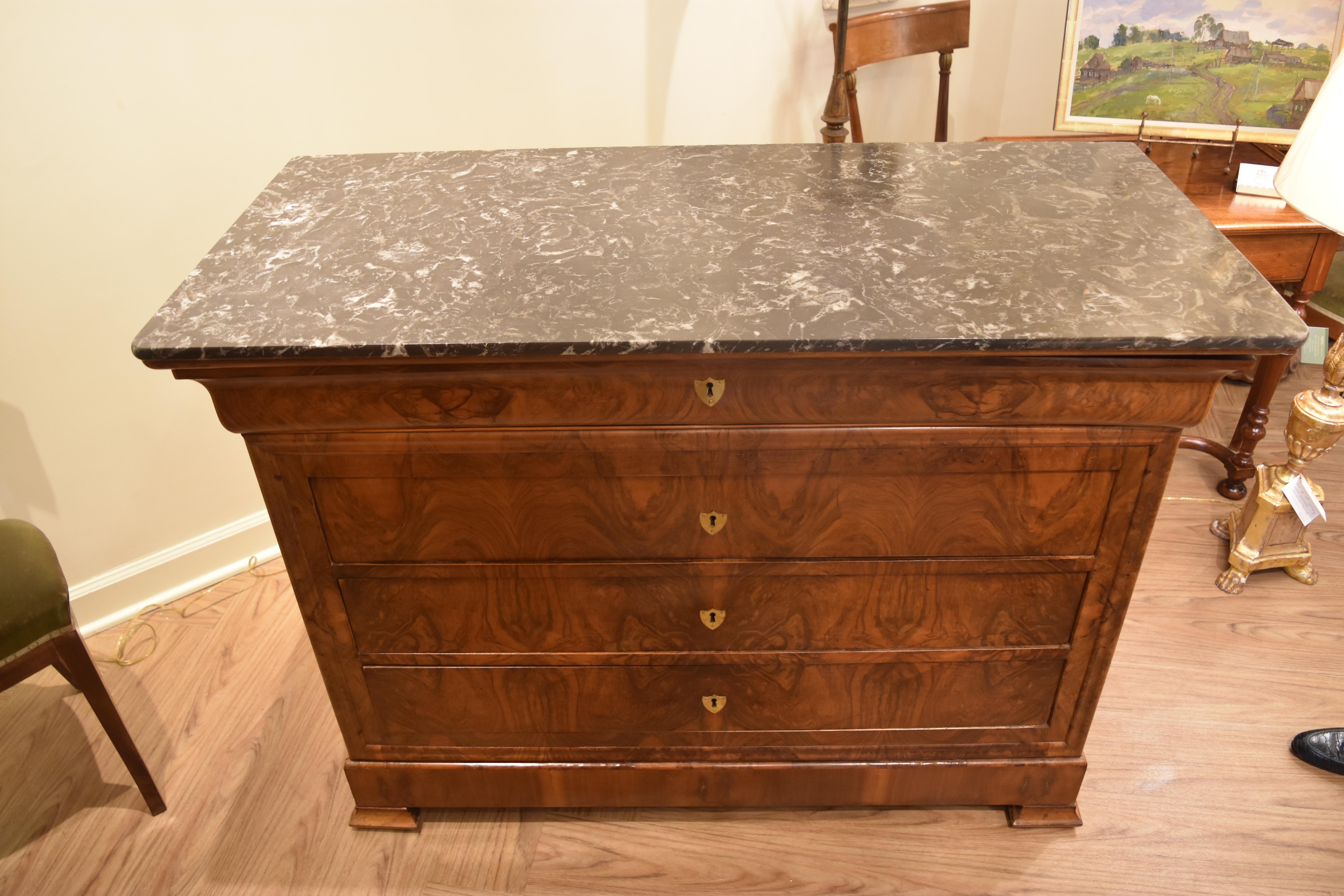 This 19th century Louis Philippe walnut commode features veneered book matched figured walnut on the facade with four working dovetailed drawers when using the key included. The top is a charcoal gray marble with white veining. Overall, this piece