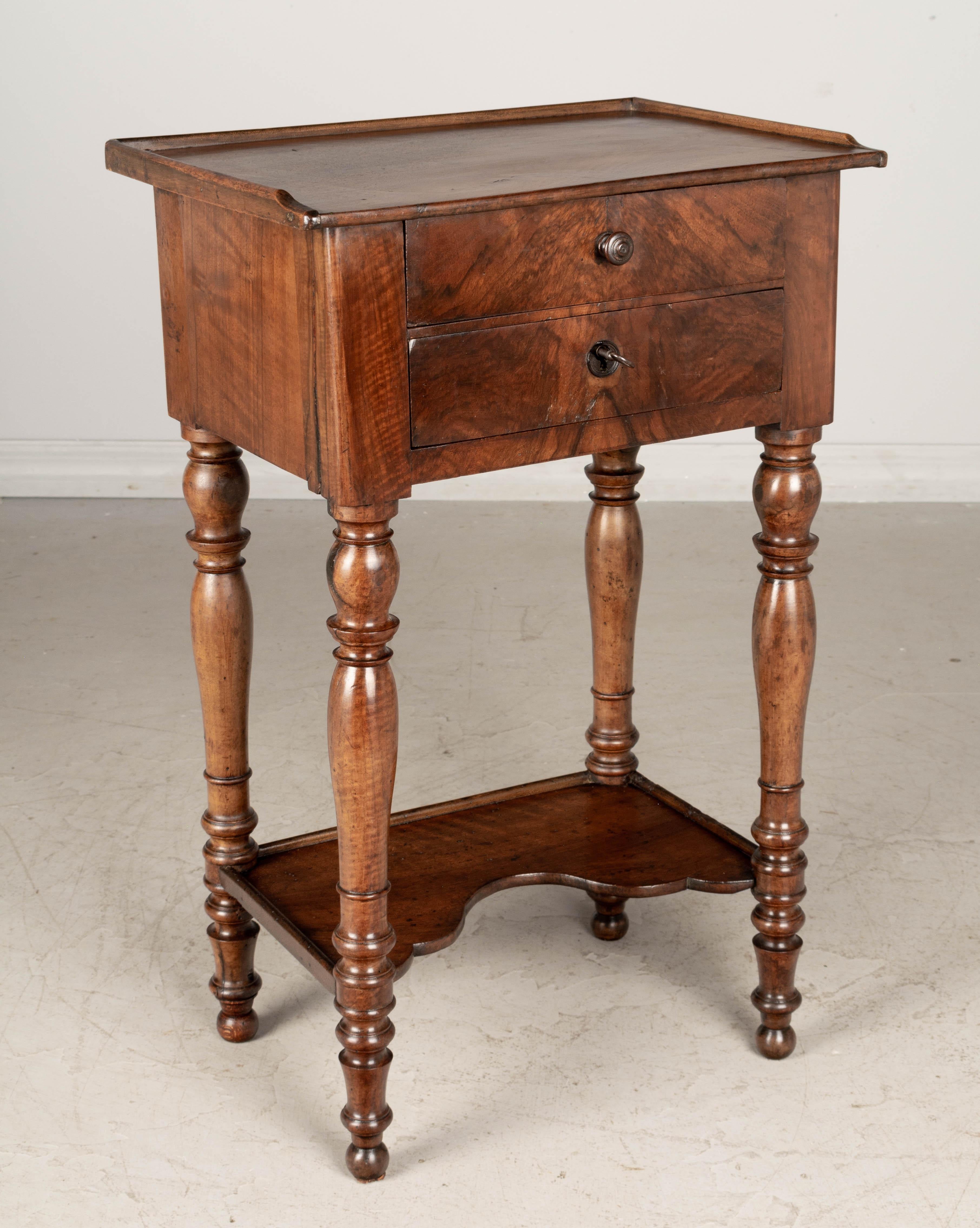 A 19th Century Louis Philippe walnut side table with two dovetailed drawers, turned legs and a lower shelf. Beautiful woodgrain with book-matched drawer face. Finished on all four sides. Top drawer has small wood knob and bottom drawer has a working