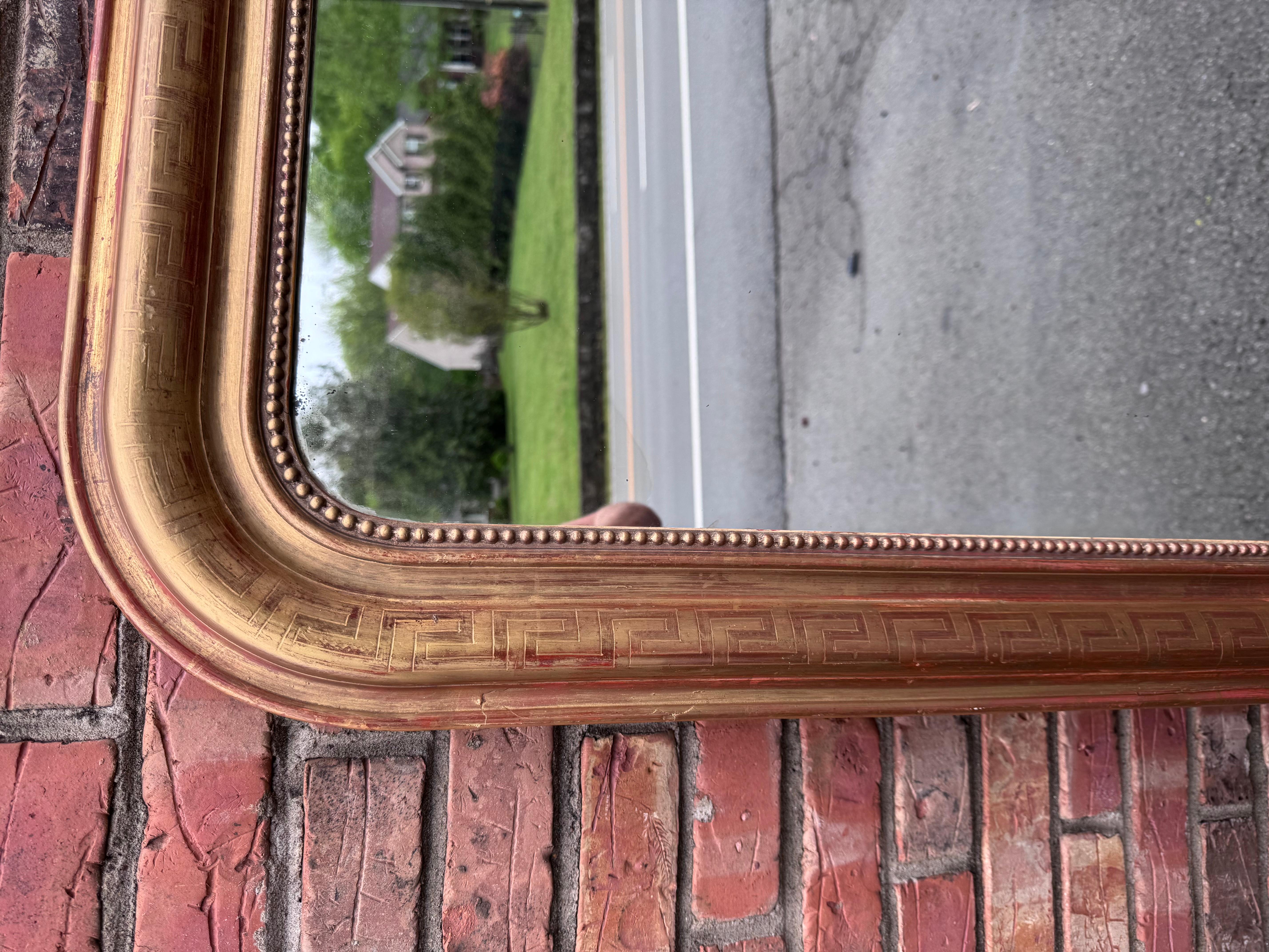 Il s'agit d'un magnifique miroir Louis Philippe dont le cadre en bois massif doré présente de subtiles nuances de rouge. Cependant, des détails délicats sur les bords ajoutent une touche d'ornementation. Ce miroir est unique en ce sens qu'il s'étend
