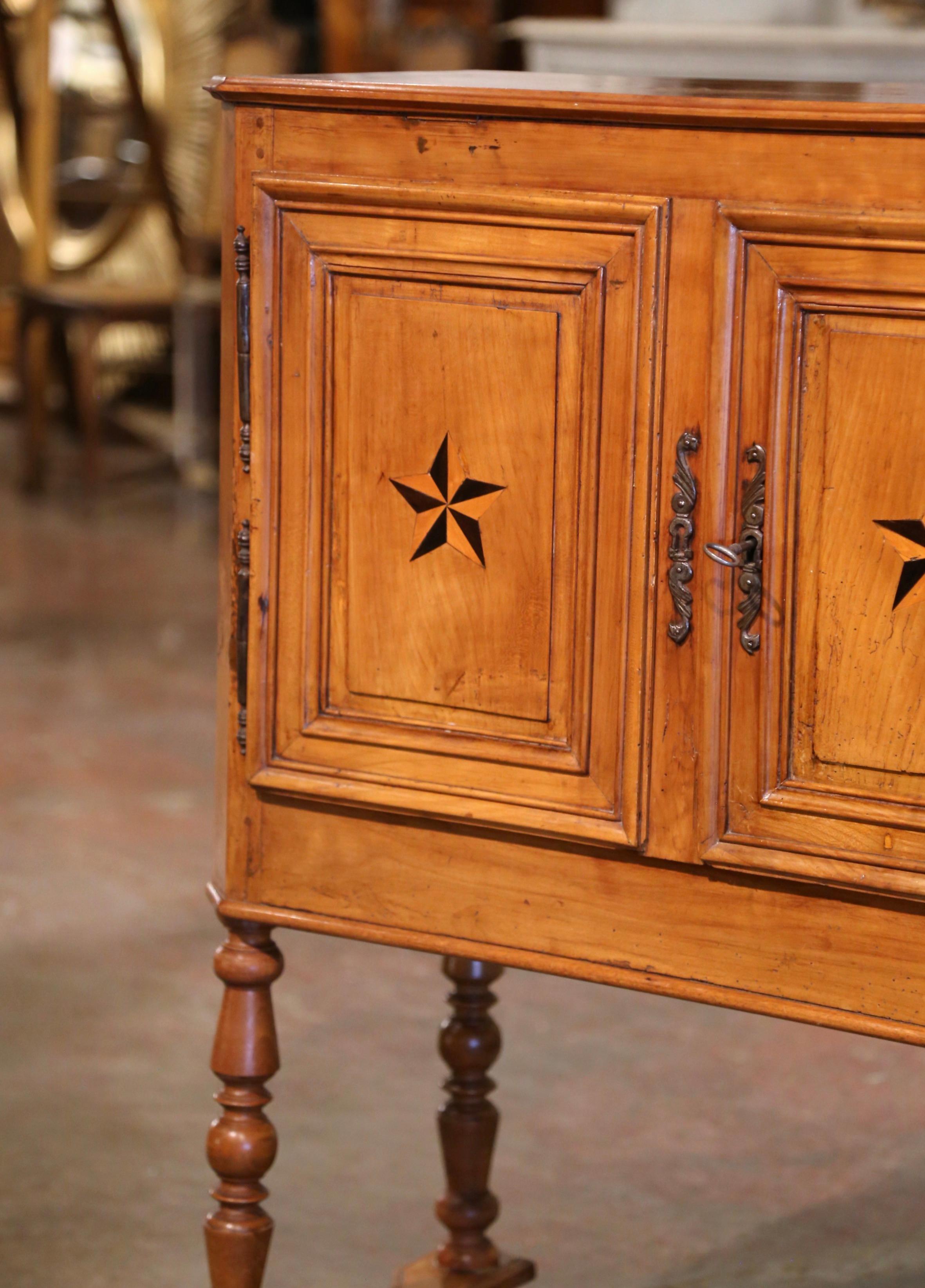 This elegant antique cabinet was crafted in the Poitou region of France circa 1820. Built of cherry wood and oak wood, the buffet stands on turned legs ending with a cross stretcher at the base. The cabinet features two doors decorated with inlaid