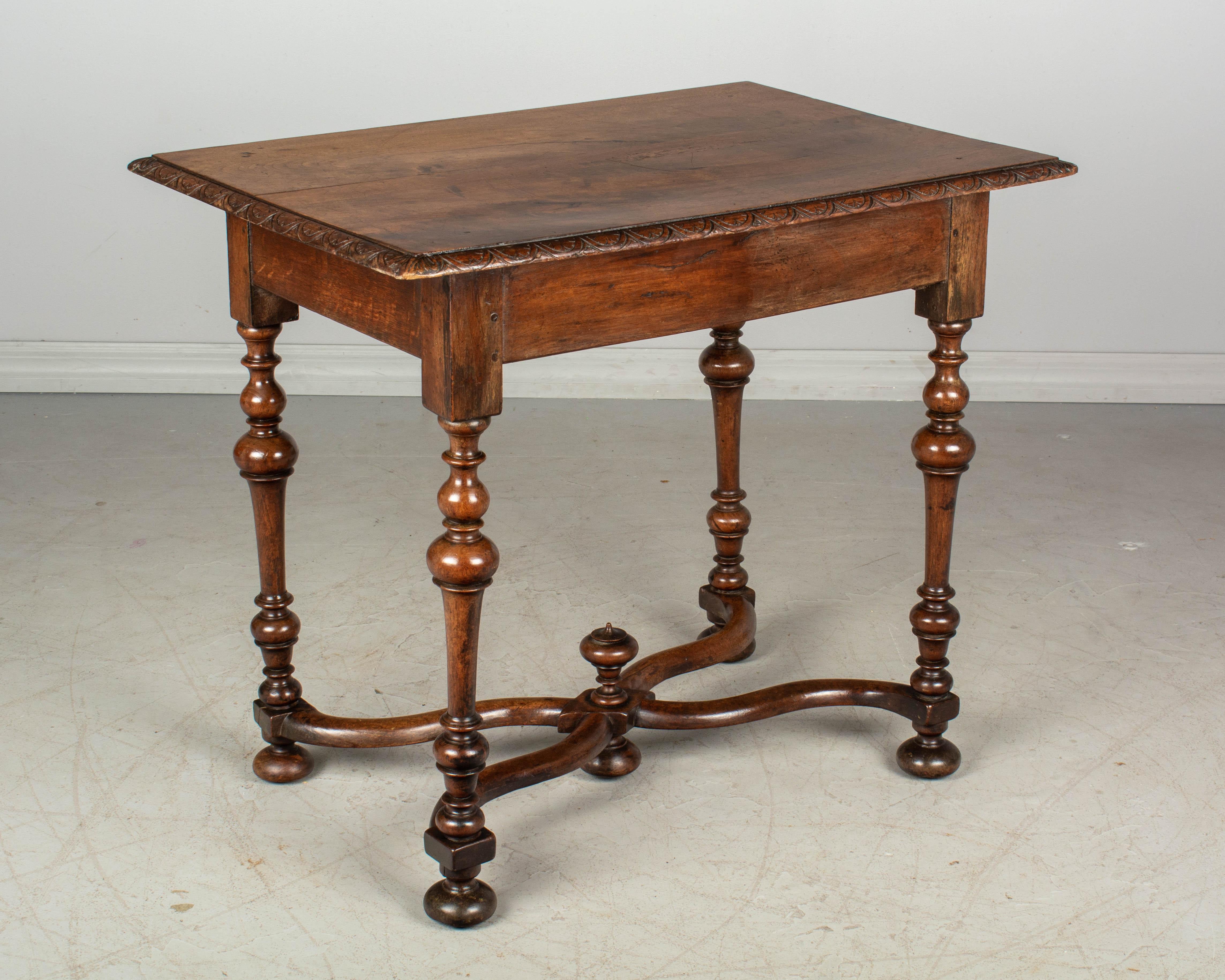 A 19th century Louis XIII style French side table made of solid walnut with a large dovetailed drawer. Fine turned legs and X-form stretcher with center finial. Pegged construction. Waxed patina. All original. This type of table was used as a