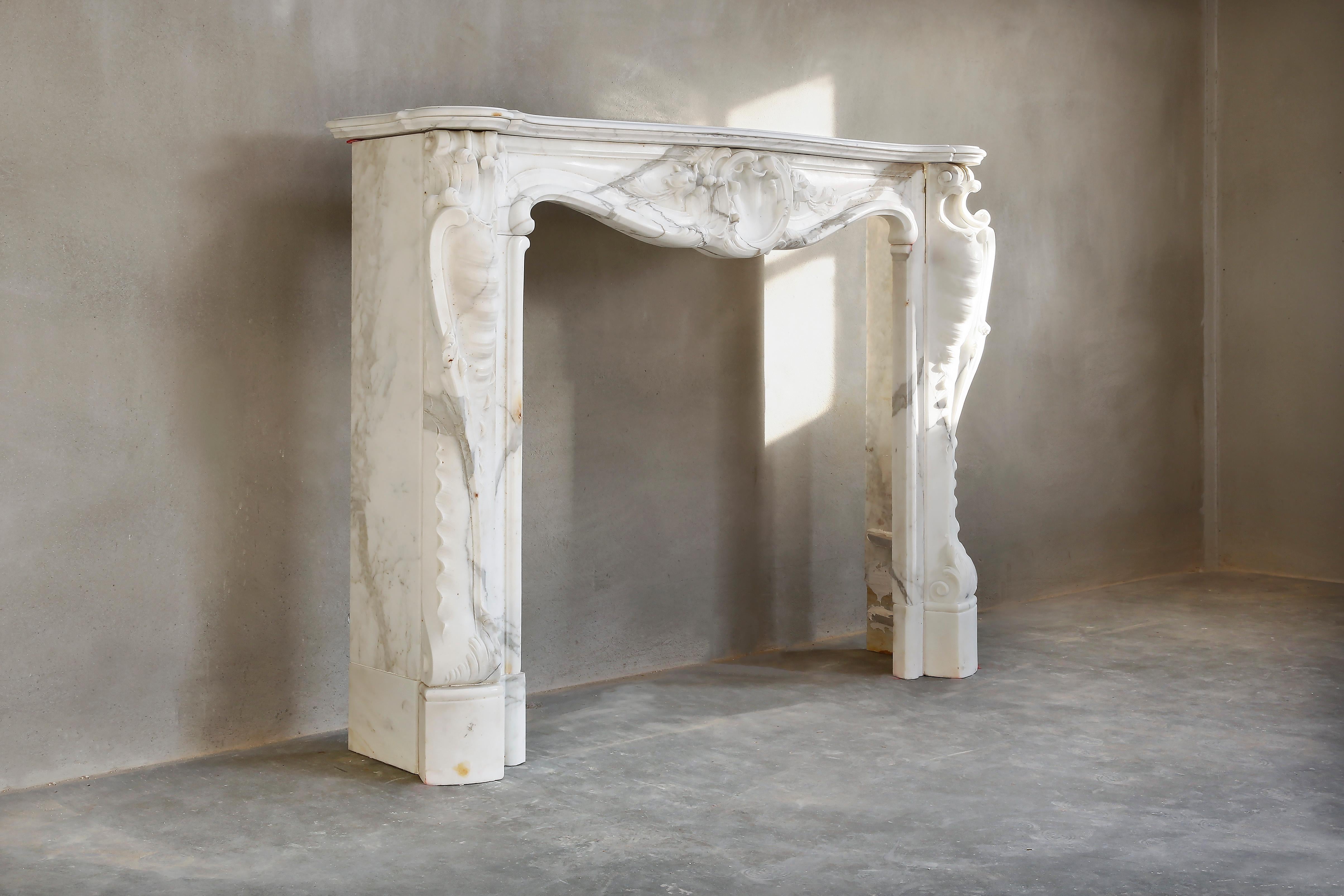 A very beautiful antique fireplace made of statuario marble. This type of marble comes from Italy and has light veins. The fireplace dates from the 19th century and is in the style of Louis XV. This type of fireplace is often equipped with a scallop