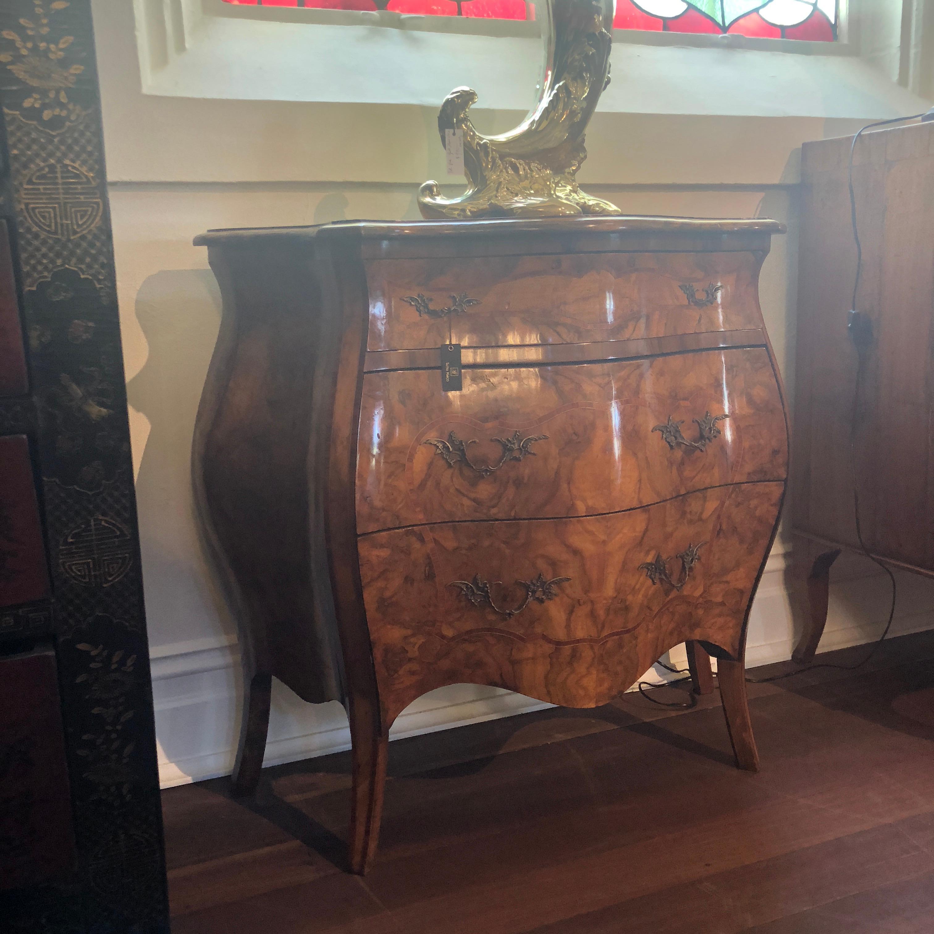 This exceptional burl walnut bombe commode features the most spectacular marbled patina, accentuating its beautiful, curved 'bombe' shape. Six original brass drawer pulls adorn the front of this piece with simple bordered inlay on the front, each