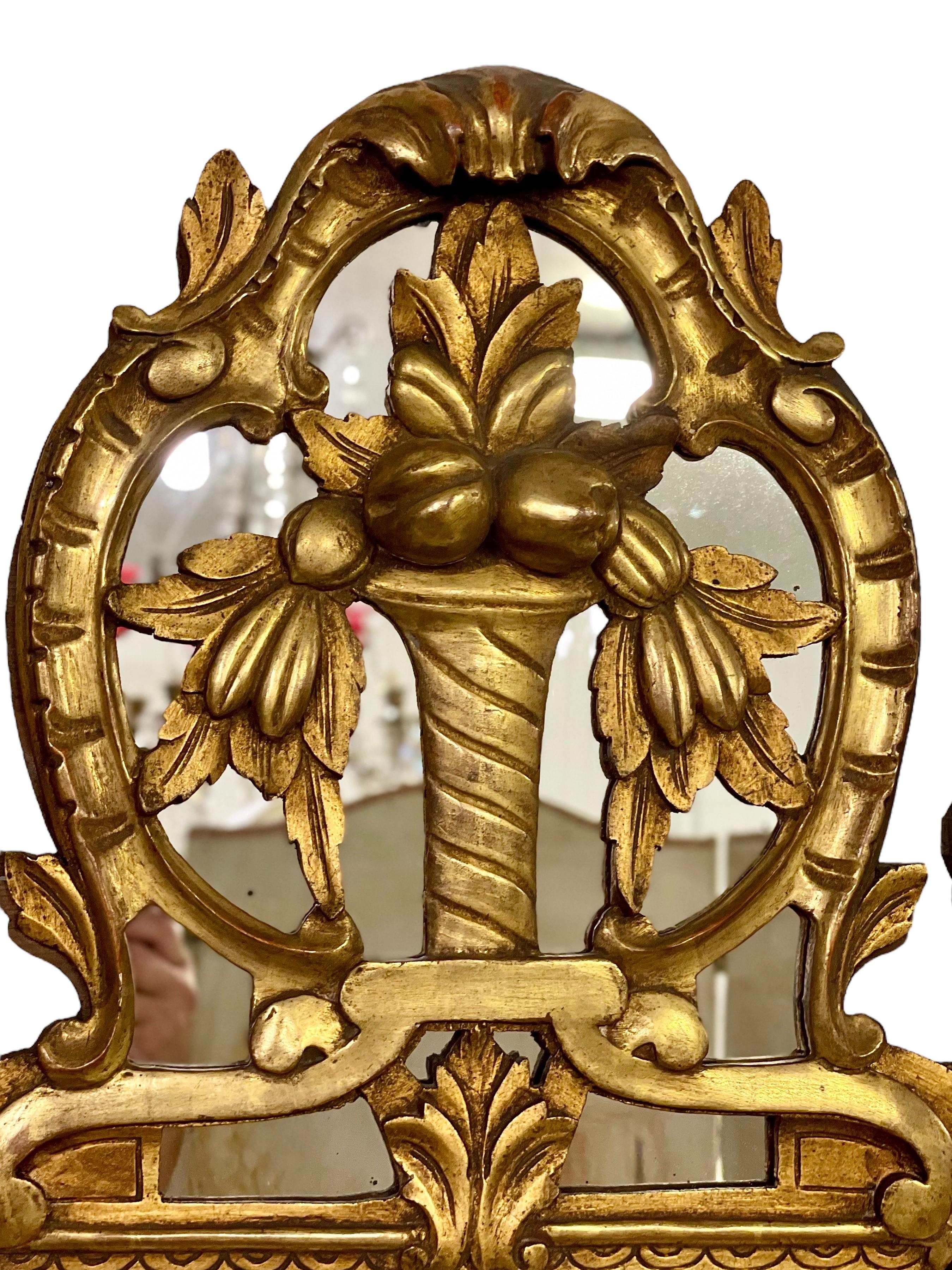 Ce superbe miroir mural de style Régence est délicieusement fabriqué à la main en bois doré et stuqué, et est exubérément décoré de feuilles d'acanthe, de rinceaux en C et de grappes de raisin dodues de chaque côté. La crête ajourée est décorée d'un