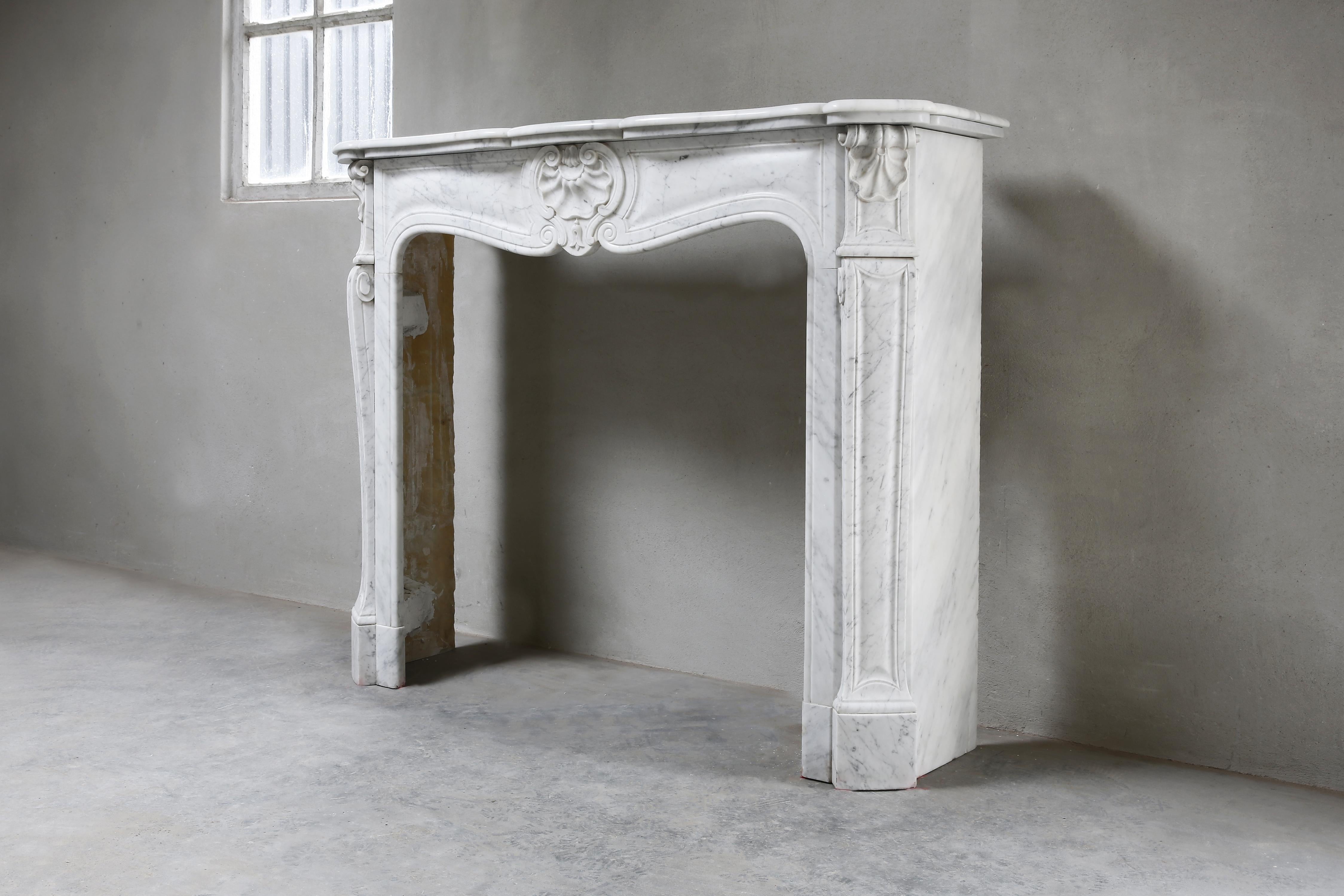 Beautiful elegant antique Carrara marble fireplace surround from the early 20th century in the style of Louis XV. This mantelpiece is decorated with a scallop in the center and on the sides. The light veins, white Carrara marble and round shape give