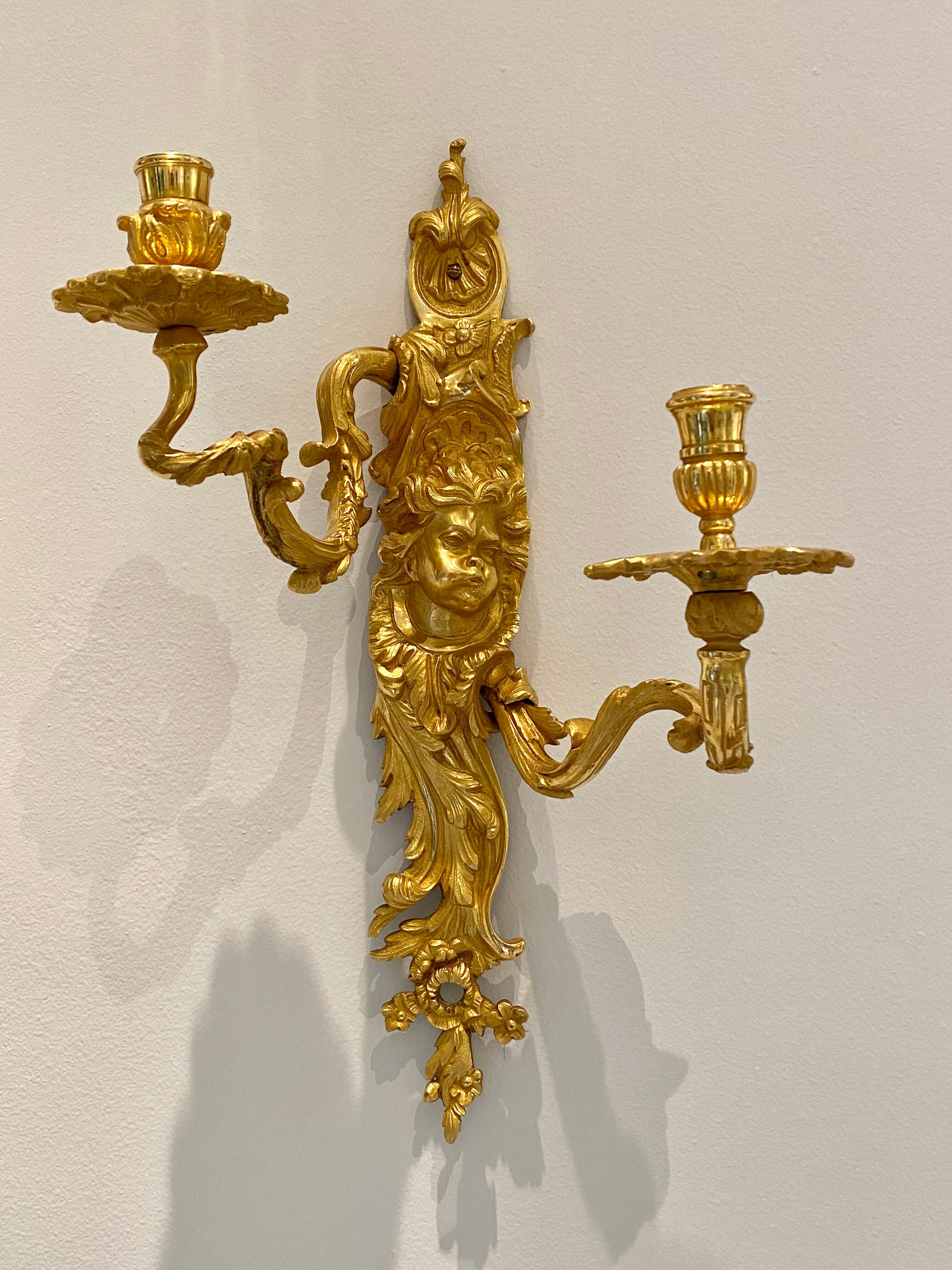 Fine pair of gilded and sculpted ormolu  bronze sconces in Louis XV style. They each feature two arms that wind out from the stem and upward like branches. Each stem is richly decorated with scrolling foliage, shells, flowers, and cherubs'