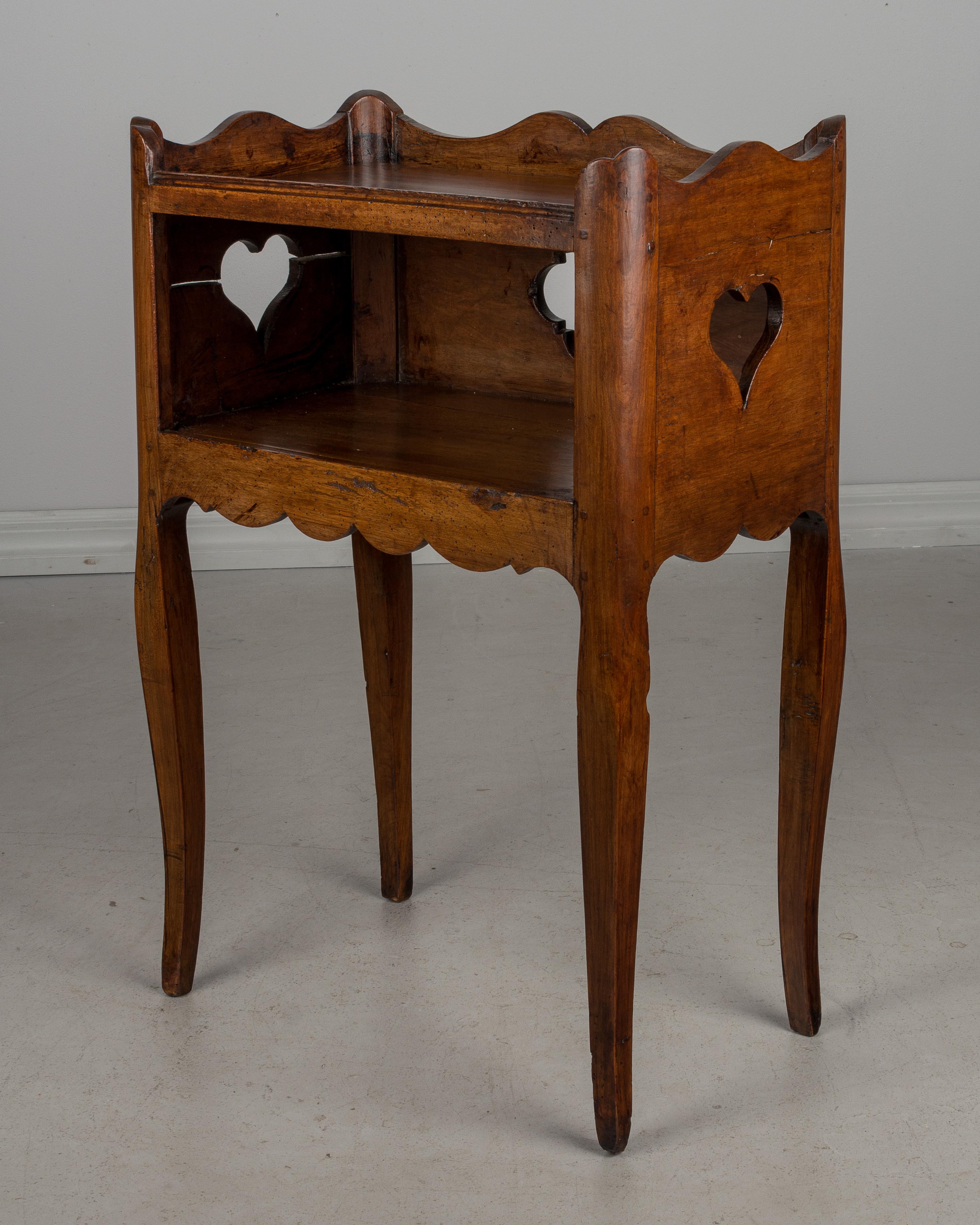 An early 19th century Louis XV Country French side table or nightstand made of solid walnut, with a pierced quatrefoil shaped cut-out on the back and hearts cut-out on the sides. Scalloped apron and gallery surrounding the upper shelf. Slender