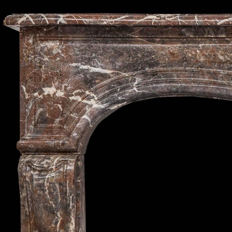 A Rouge Royal marble Louis XV antique fireplace mantel in Rococo style,
The Serpentine shelf above the paneled frieze centered by a large floral cartouche and supported on straight double paneled jambs.