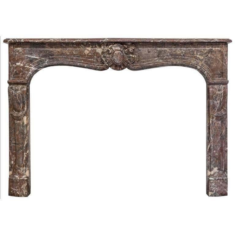 A Rouge Royal marble Louis XV antique fireplace mantel in Rococo style, The Serpentine shelf above the paneled frieze centered by a large floral cartouche and supported on straight double paneled jambs.