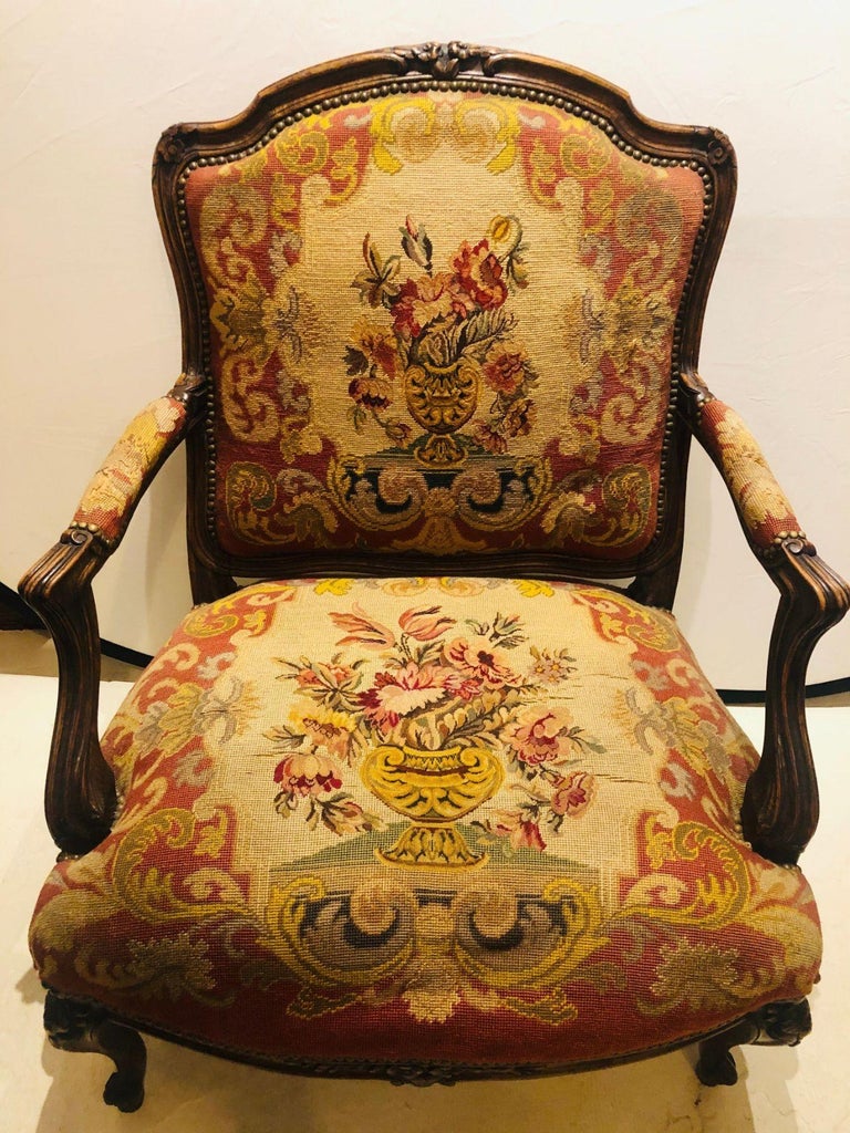 A 19th century Louis XV style armchair or bergere. The fine petite and gros needlepoint upholstery seat and backrest depicting large floral baskets or urns in vibrant colors on a wonderfully carved walnut frame. This magnificent example of opulence