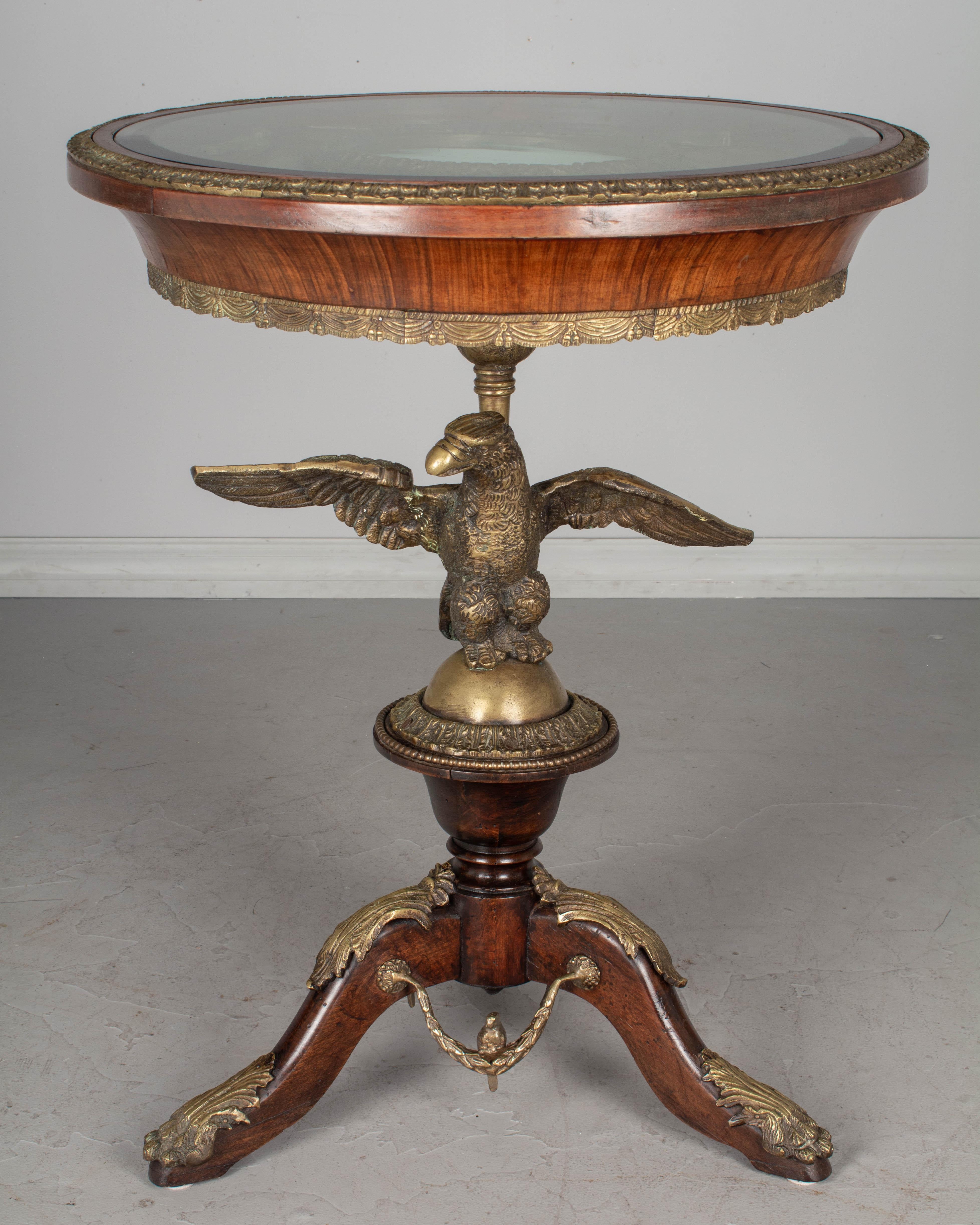 A French Louis XV style bronze mounted guéridon with a large cast bronze eagle perched on an orb in the center of the tripod pedestal base. The circular top has a hand painted Sèvres style porcelain plaque with romantic pastoral scene, signed E.