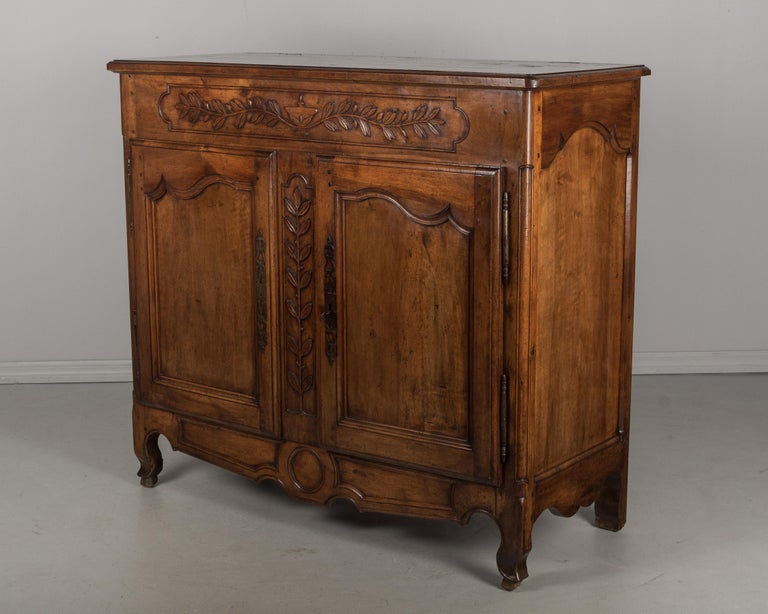 A large early 19th century Louis XV style French buffet from Provence made of solid walnut. Beautiful character to the wood and fine hand-carvings of an urn and olive branches. An unusual tall size, this buffet once had a dough box (the box is
