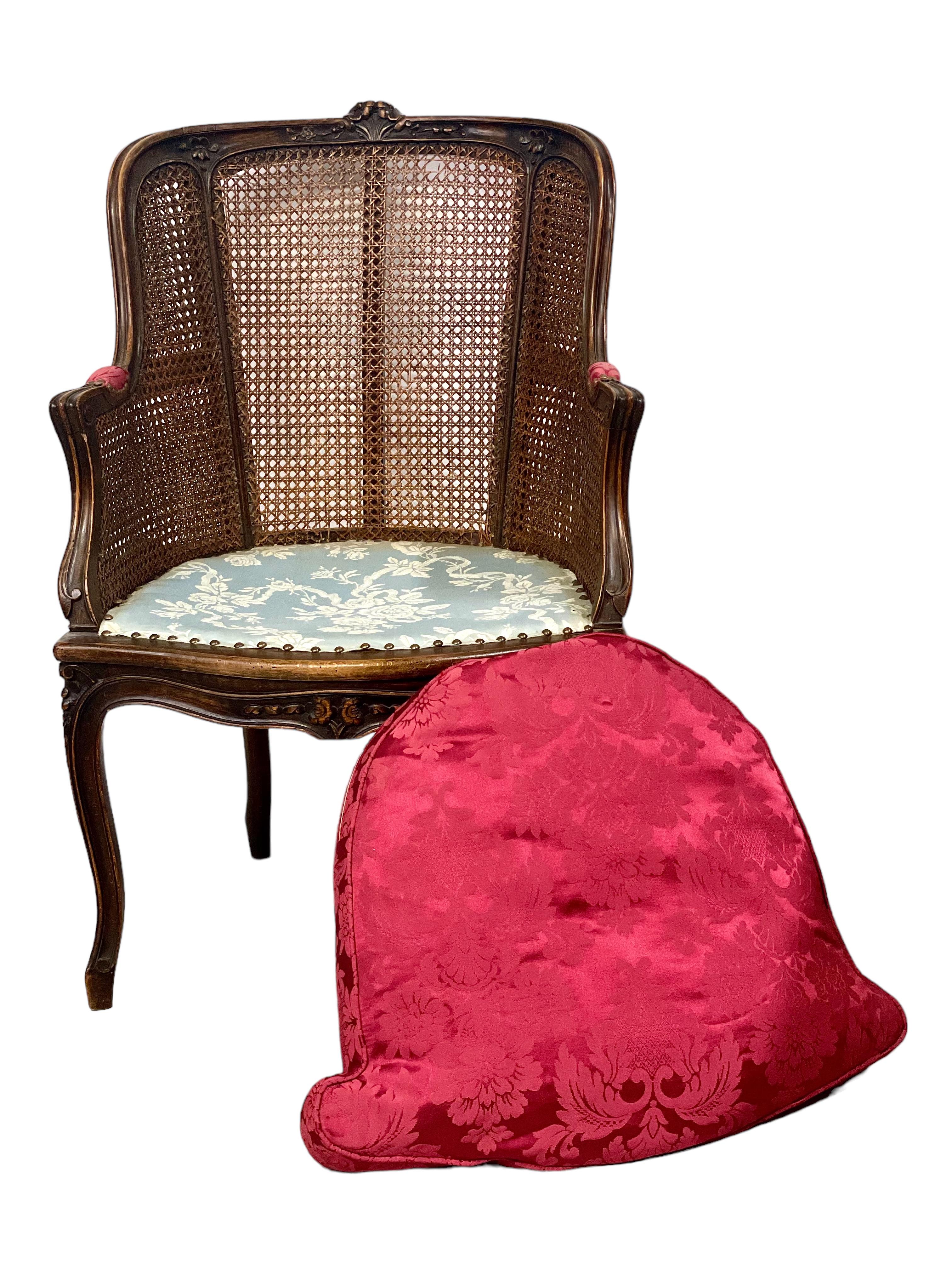 A stylish Louis XV-style caned Bergère armchair in natural wood, featuring a generously wide seat with detachable crimson plush cushion woven with an exuberant floral design. The shaped top rail has been beautifully embellished with exquisite floral
