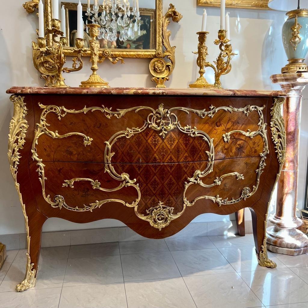 We present you this large ornamental transition Louis XV-style chest of drawers in exquisite floral marquetry, dating from the Napoleon III era. It features two drawers without a crossbar as well as a curved front and sides standing on cabriole