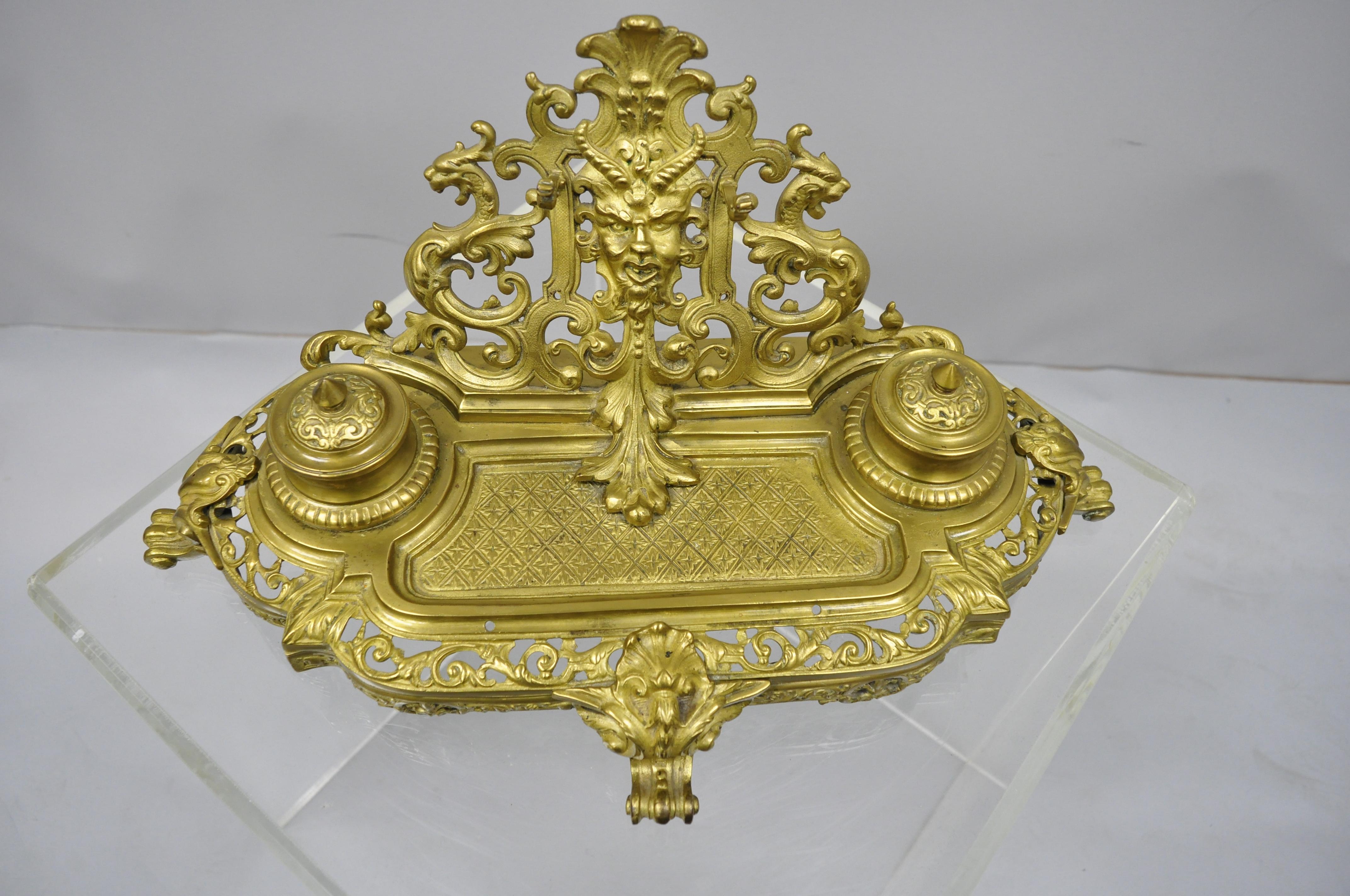 19th century, French Louis XV style figural cast bronze double inkwell pen holder. Item features cast bronze lions and central face, double inkwell with glass inserts, pen holder, and other ornate pierced bronze detail. circa 19th century.