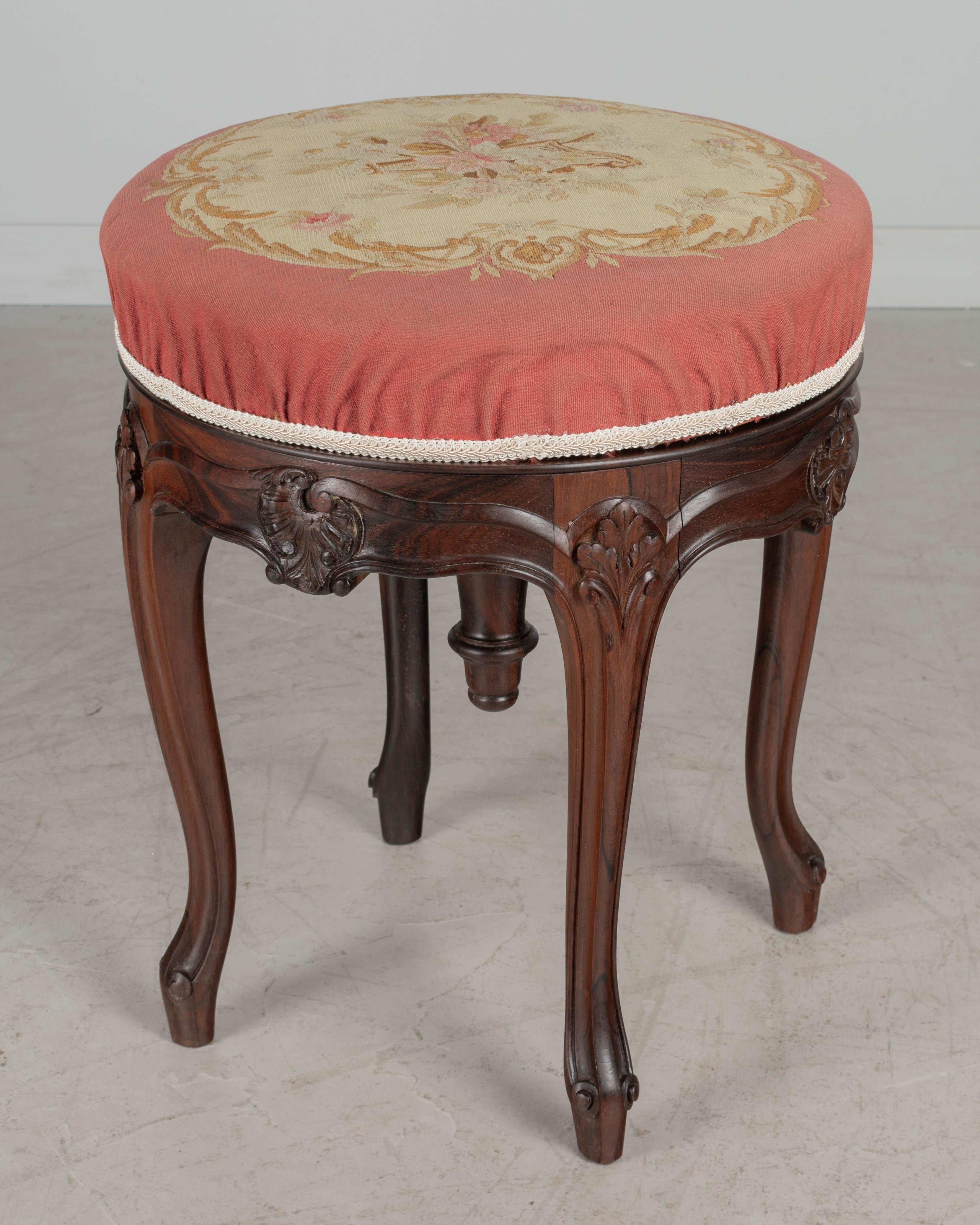 A 19th century French Louis XV style adjustable swivel stool made of solid rosewood with hand-carved details, sturdy curved legs and decorative wood finial.  Covered in original petit point tapestry fabric, depicting a harp with pink flowers. The