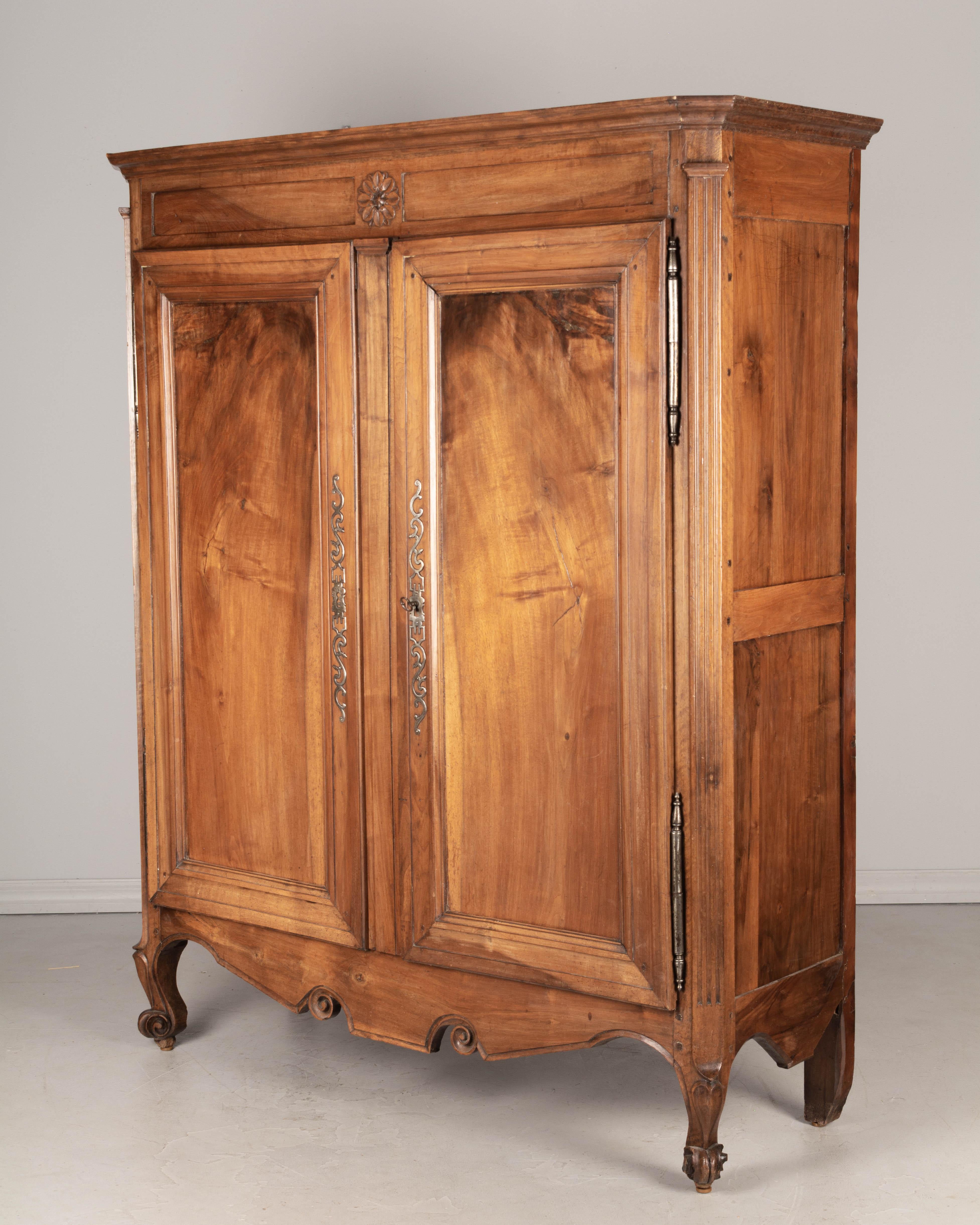 A 19th century Louis XV style French low armoire, or wardrobe, from the Loire Valley. Made of solid walnut with beautiful character to the book matched planks on the doors. Scroll carving on the apron and front feet. Original iron hardware with