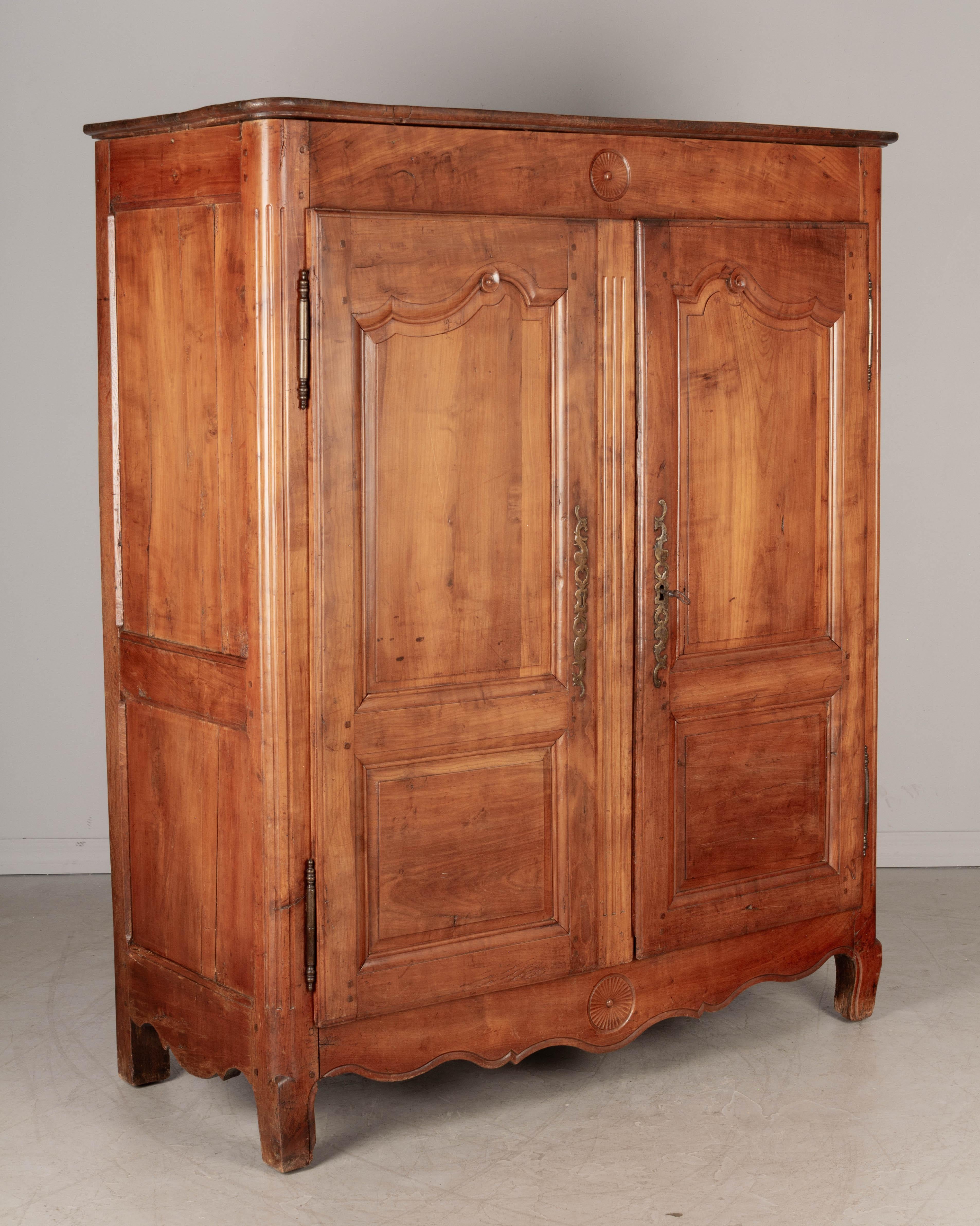An early 19th century Louis XV style French petite armoire, or wardrobe, from the Loire Valley. Made of solid cherry with scroll carving on the door panels and simple circular carved details at the top and on the apron. Original iron hardware and