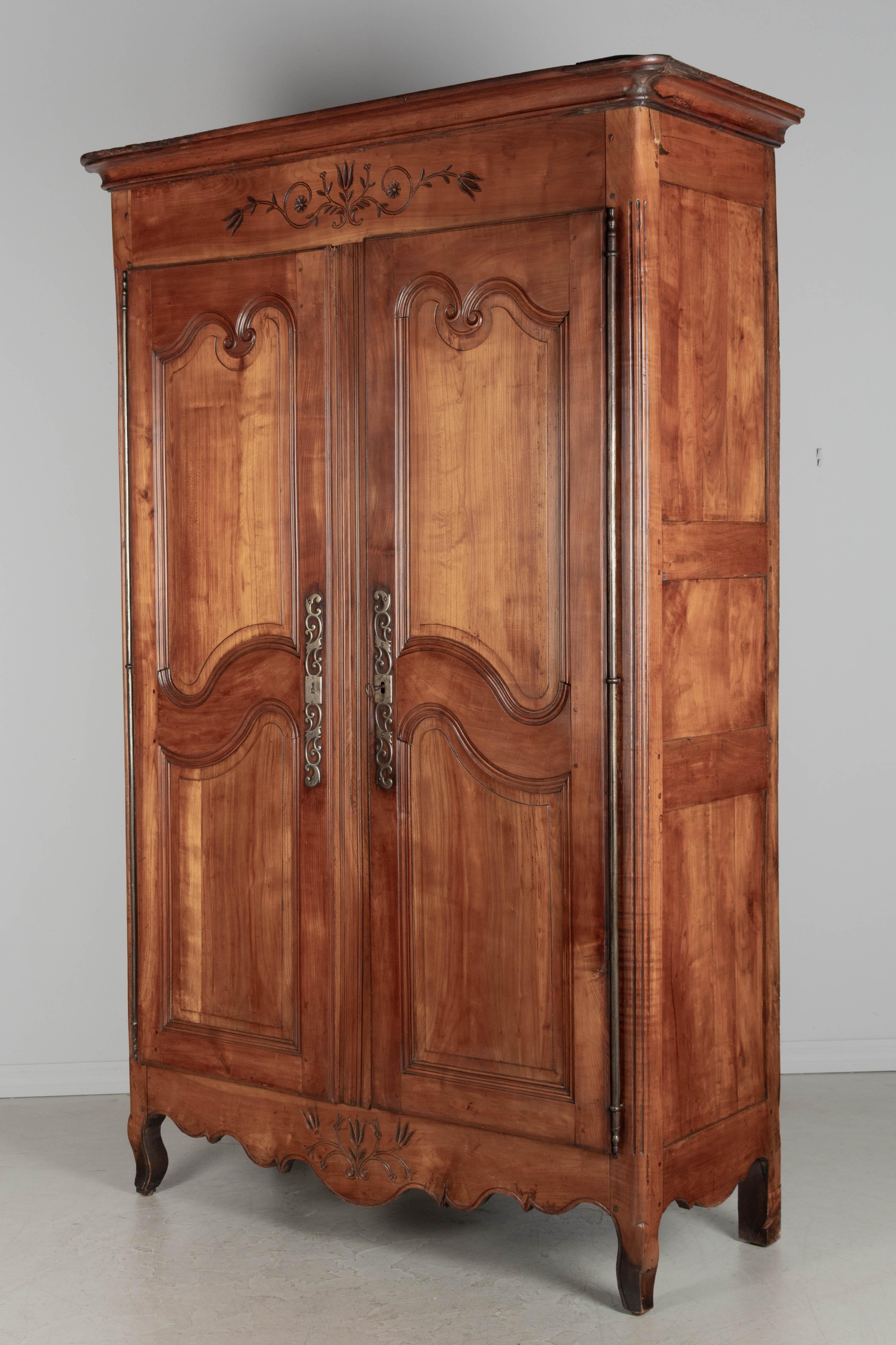 Ein französischer Kleiderschrank im Stil Louis XV aus dem 19. Jahrhundert aus dem Loire-Tal. Aus massivem Kirschbaumholz mit Schnitzereien an den Türflügeln und einfachen Schnitzereien an der Oberseite und an der Schürze. Originale Eisenbeschläge