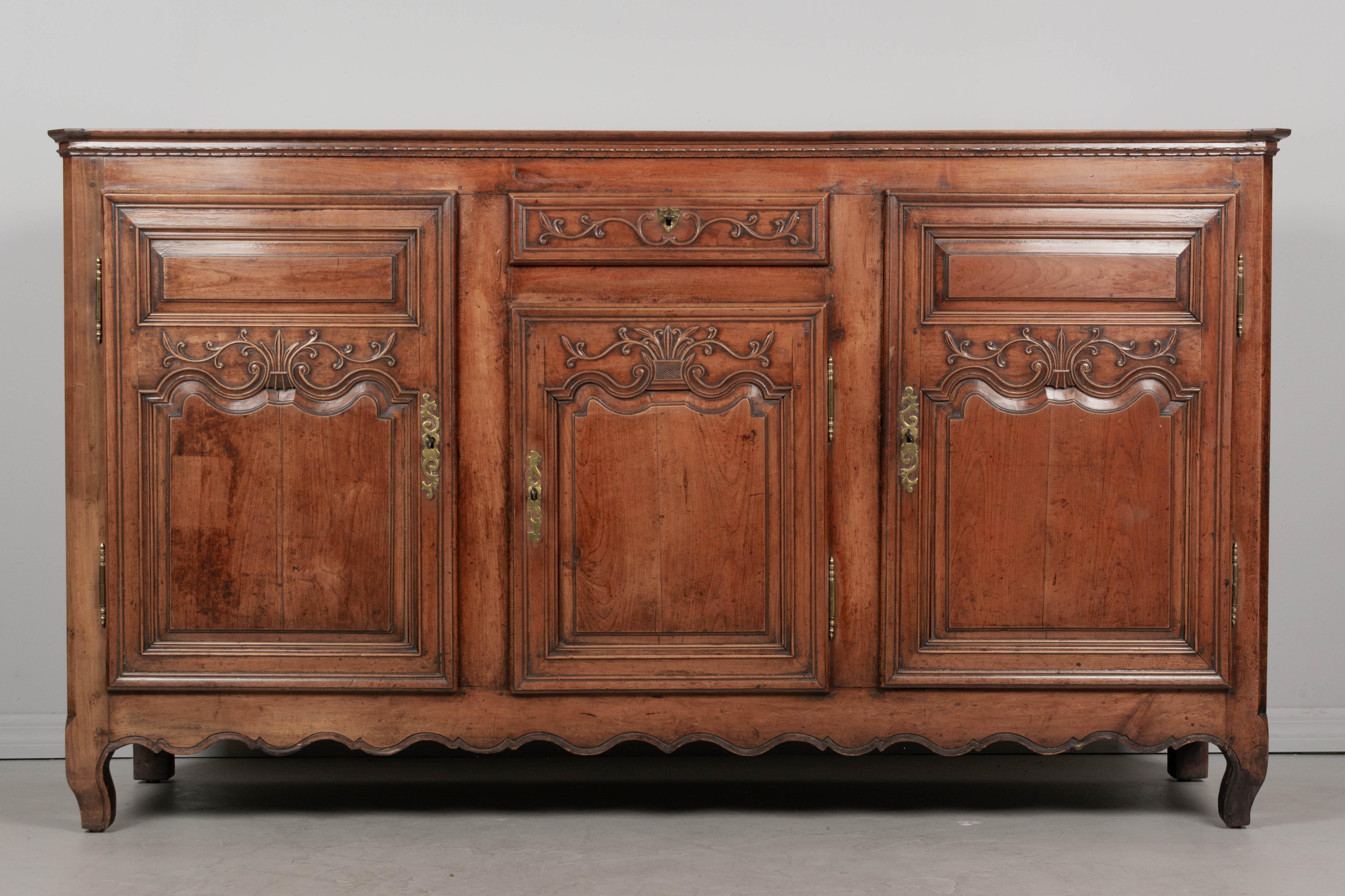 Un'enfilade, o credenza, in stile Luigi XV del XIX secolo, proveniente dalla Piccardia, nel nord della Francia. Realizzato in legno massiccio di ciliegio con dettagli intagliati a mano. Tre  porte con serrature e chiavi funzionanti e un cassetto a
