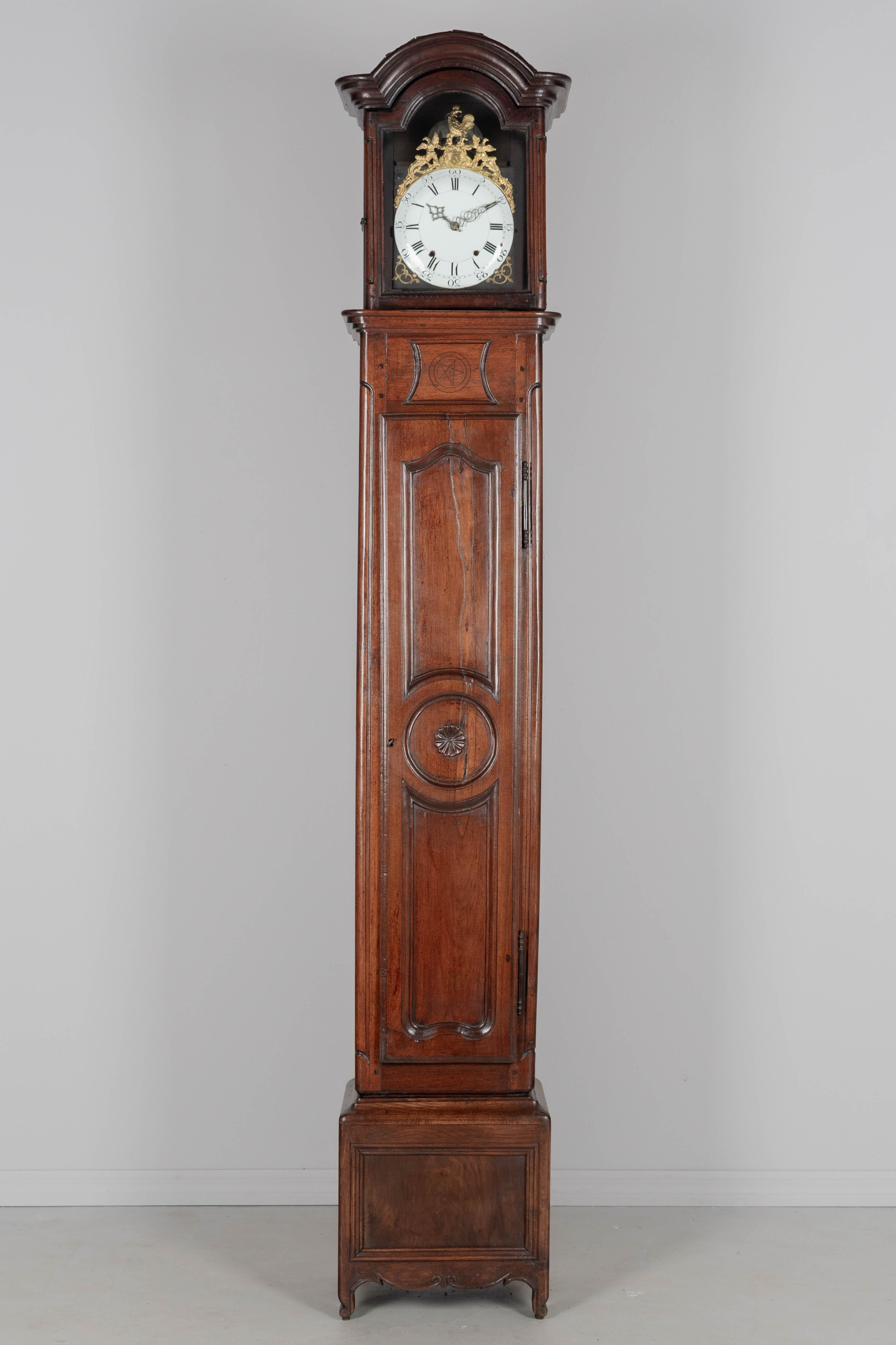 A 19th century Louis XV style French walnut horloge de parquet, or tall case clock, in two parts. The body has a paneled door crafted from a single plank and carved with a rosette decoration. A simple five-point star is carved into the case. The top