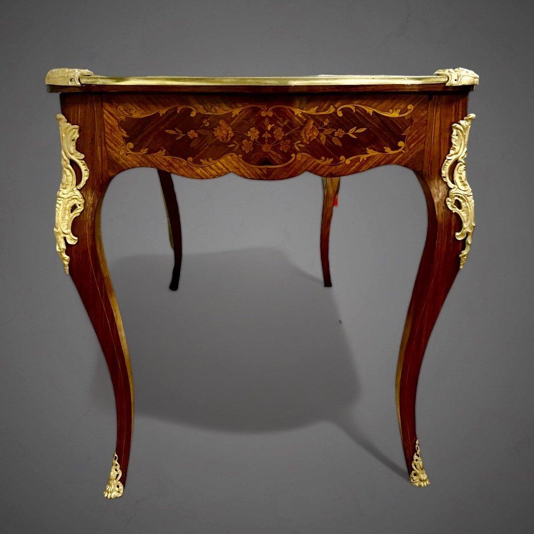This exquisite desk, designed in the Louis XV style and originating from the late Napoleon III era. It showcases meticulous craftsmanship through its rich marquetry ornamentation. It is adorned with fine details crafted in gilt bronze, showcasing