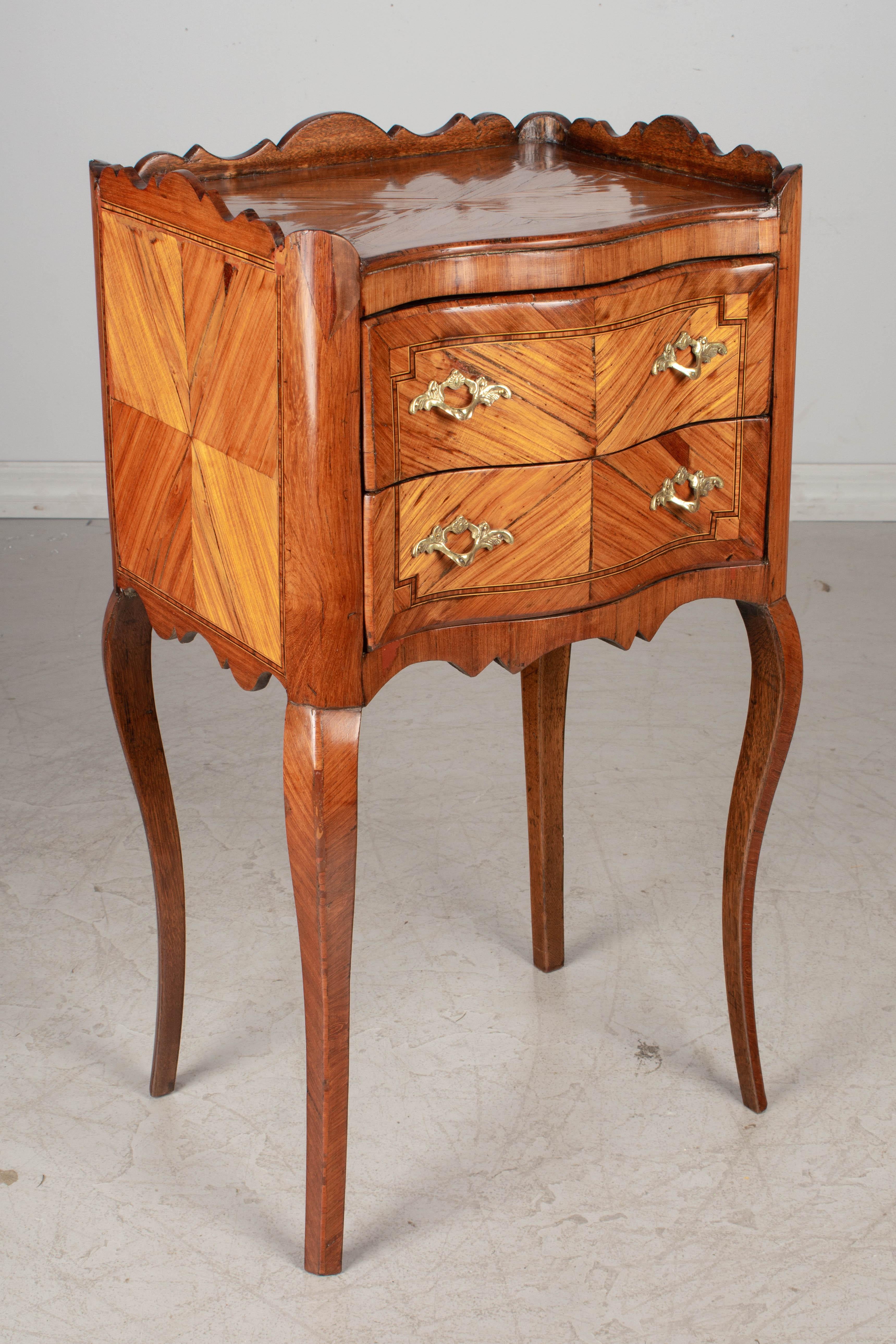 A 19th century Louis XV style French two-drawer side table, or night stand with inlaid marquetry veneers of walnut and mahogany. Cast bronze hardware. Nice proportions with curved corners and slender legs. Finished on all four sides. Some missing