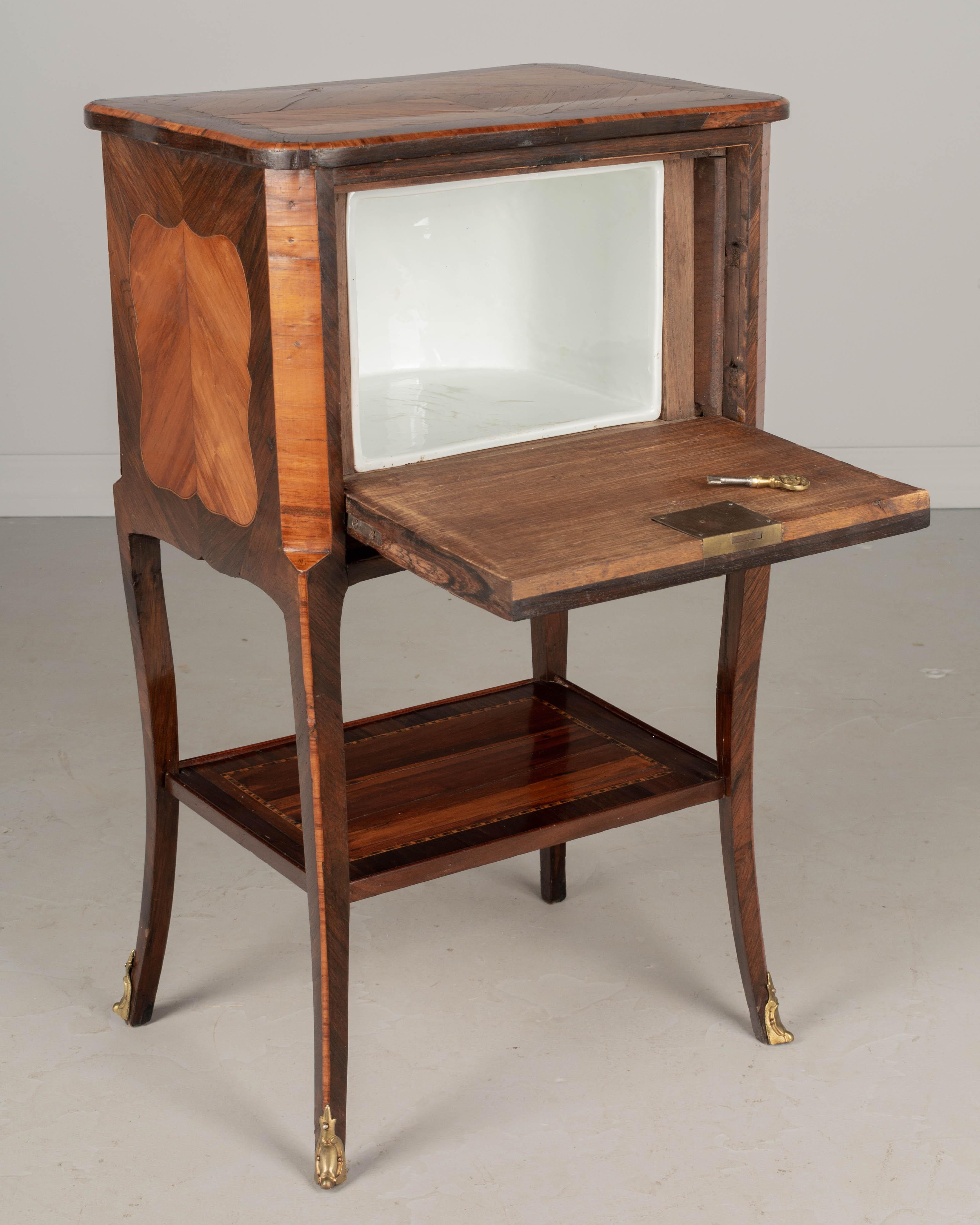 A 19th century Louis XV style French nightstand or side table with inlaid marquetry veneers of walnut and mahogany. Pull down cabinet door with false front made to look like three drawers. Cast bronze hardware with working lock and key. Interior has