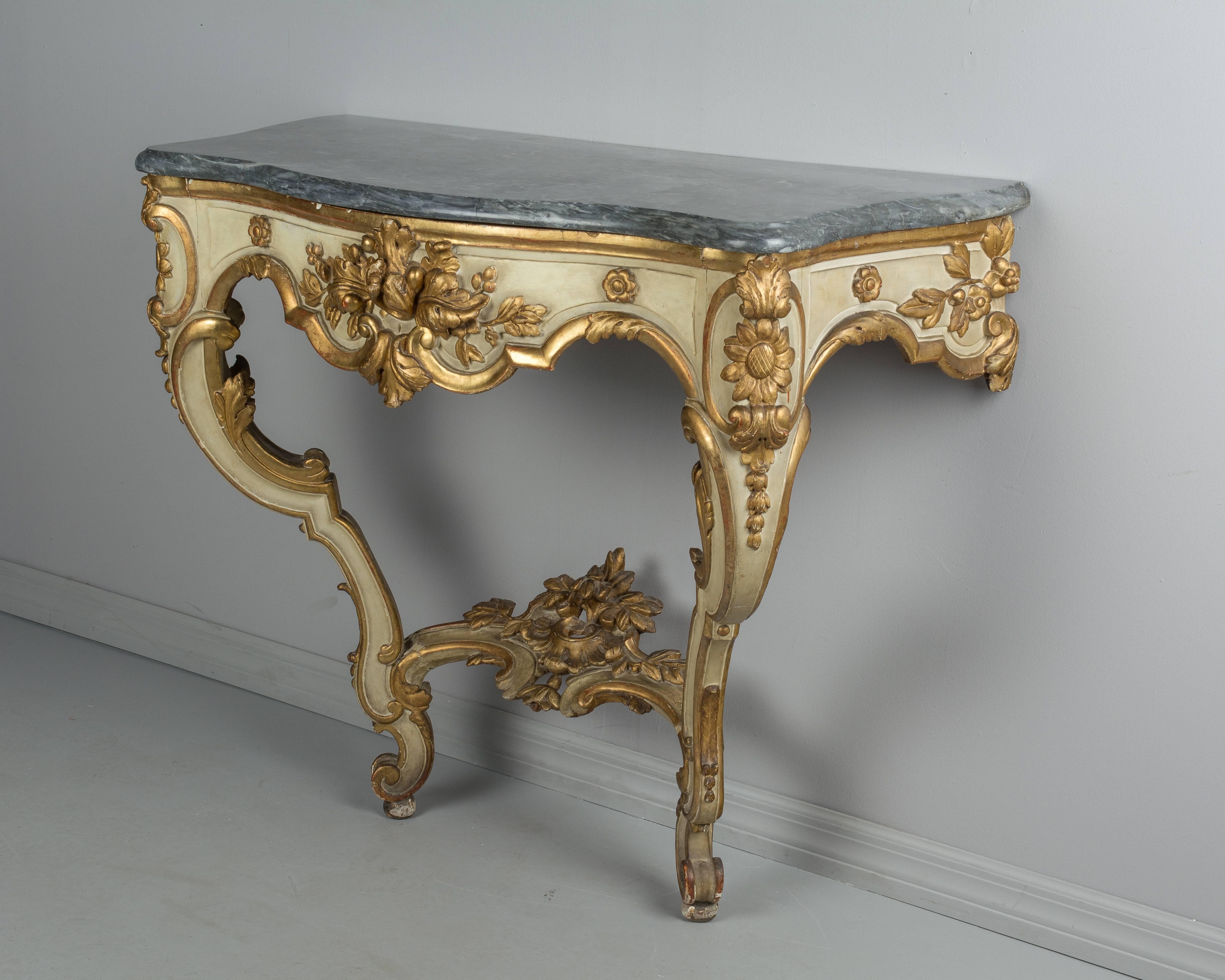 A 19th century Louis XV style parcel-gilt console with grey marble top. Richly detailed with beautiful gilded floral carvings against a pale verdigris painted surface. Bright gilt with only minor losses. Sturdy base is in excellent condition.