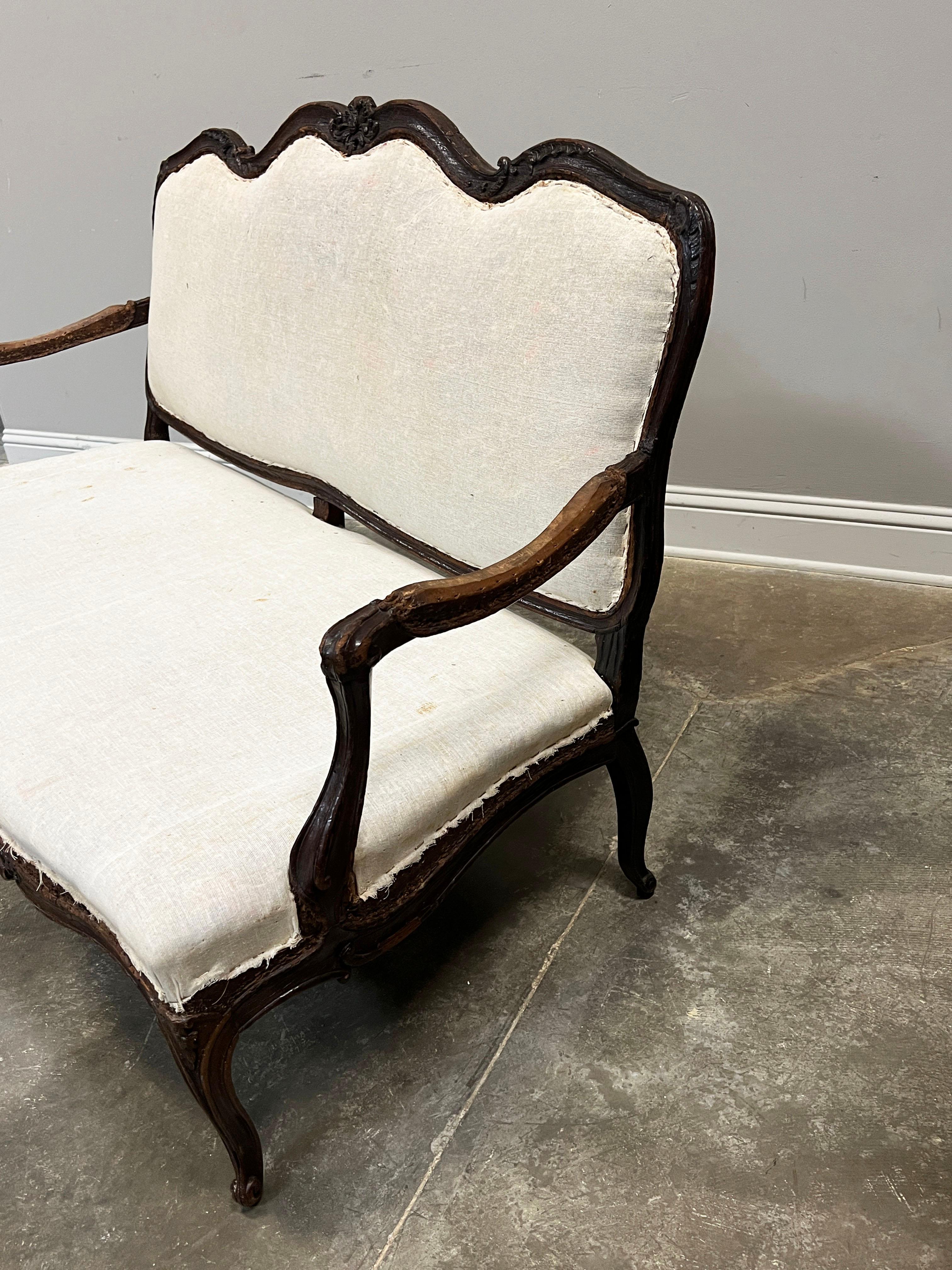 19th C. Louis XV style settee with beautifully hand carved floral motifs, scroll work arms and six cabriole legs all consistent with the Louis XV style. Upholstered in a muslin liner on the front side and original floral upholstery on the back.